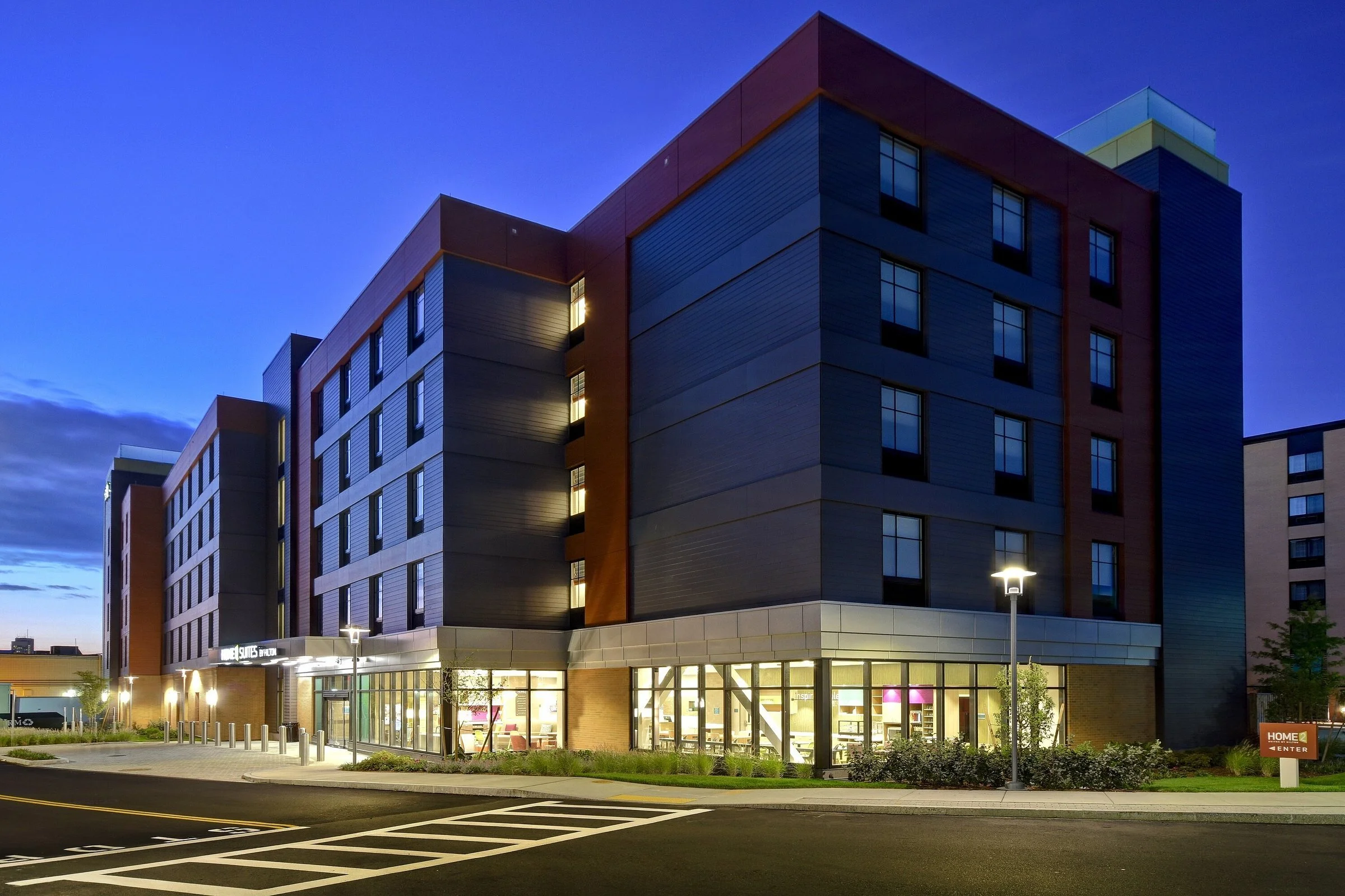 Night view of modern multi-story building with large glass windows and parking lot in front, illuminated by streetlights.