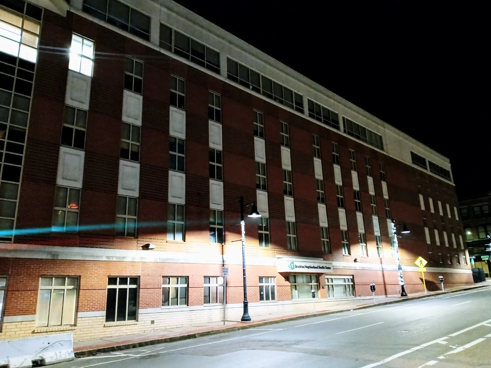 Night view of a multi-story brick building with windows, street lamps, and a sign that reads 'Erie County Neighborhood Health Center'.