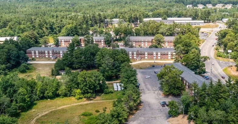 Aerial view of a residential area with multiple apartment buildings, surrounded by trees, roads, and a parking lot.