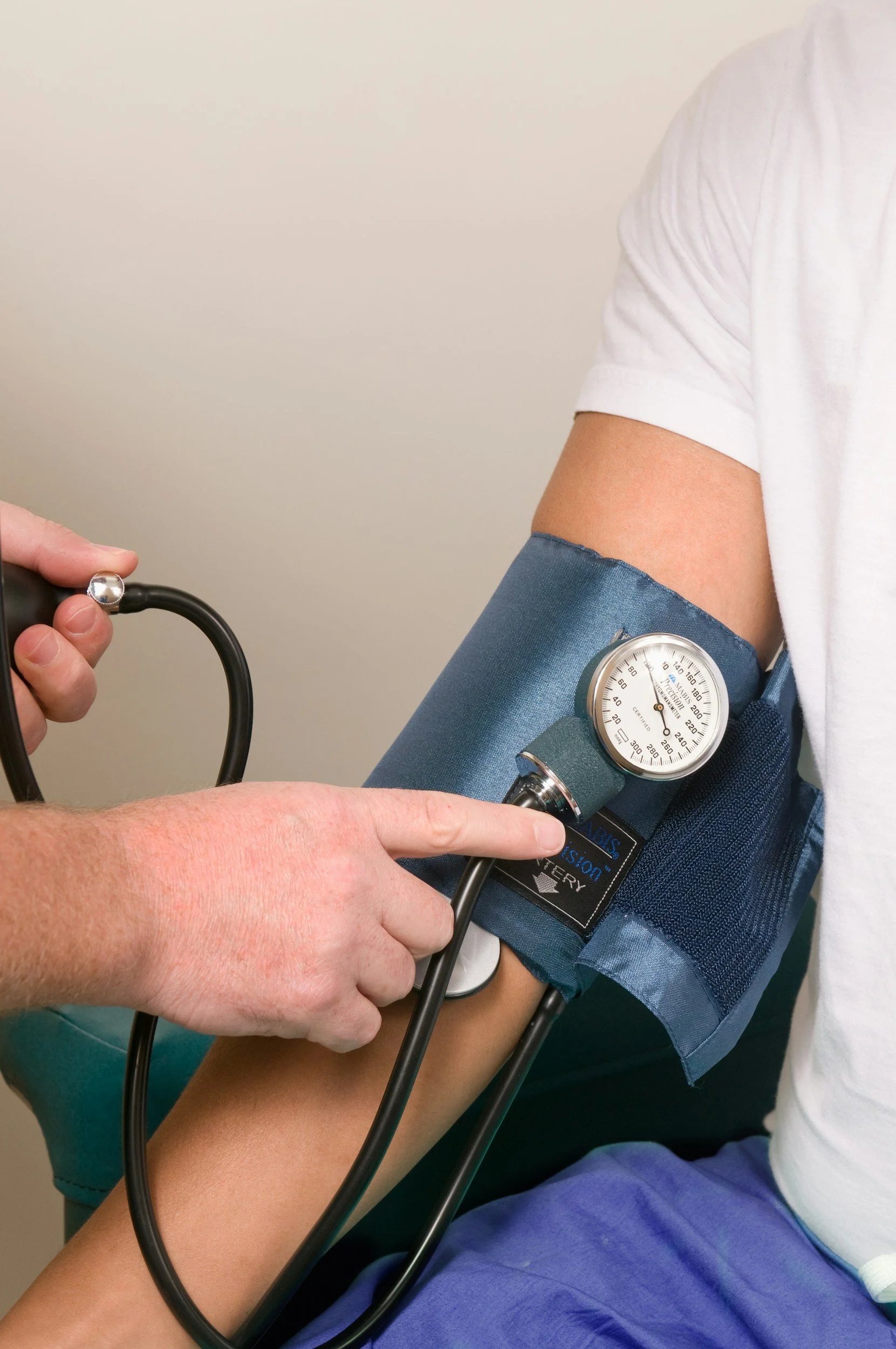 A person is having their blood pressure taken by a healthcare professional using a sphygmomanometer and stethoscope.