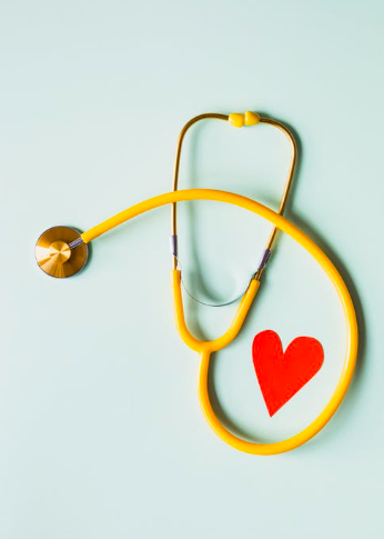 Yellow stethoscope with a red heart cutout on its chest piece, hanging on a light-colored wall.