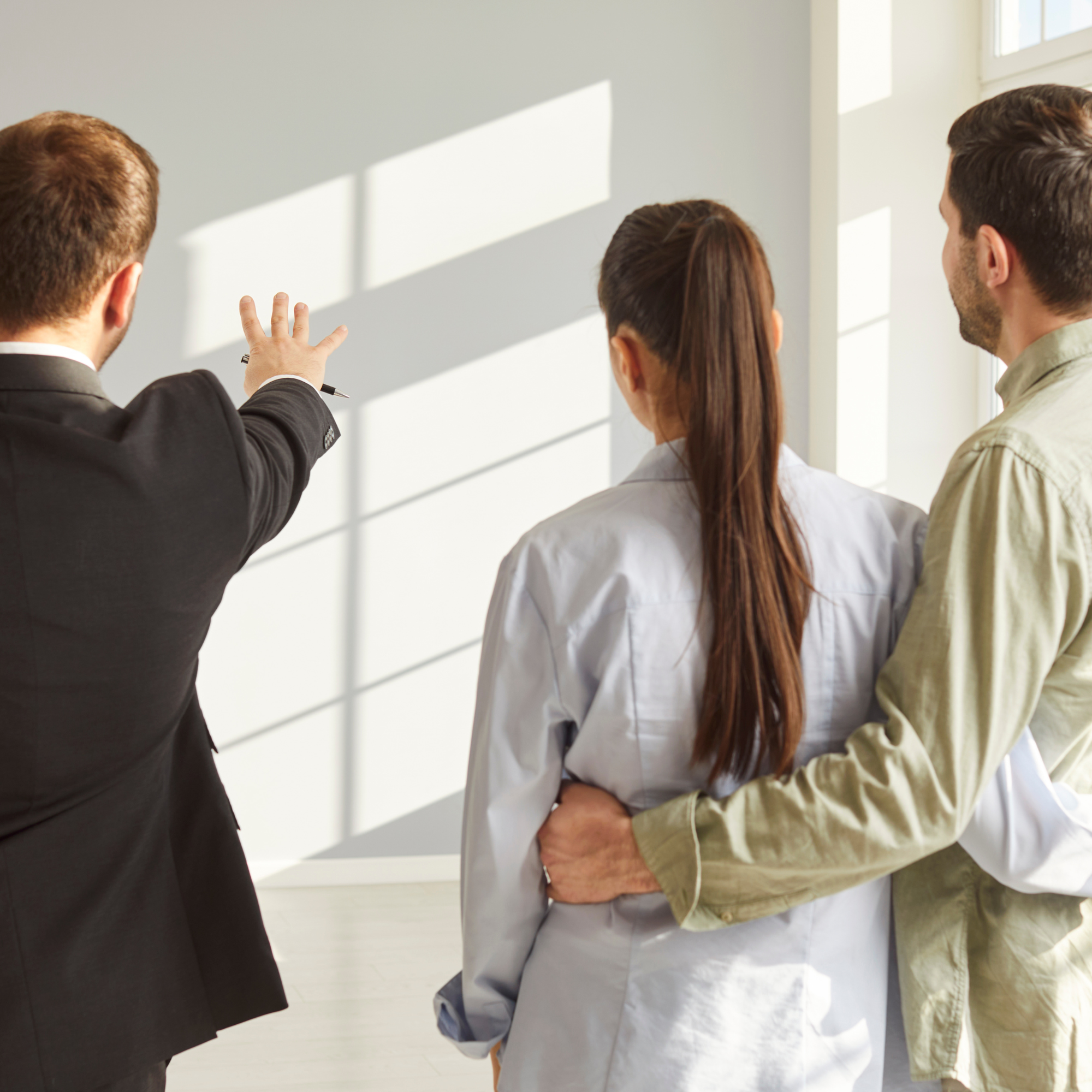 Four people, including two women and two men, engaged in a discussion in a bright room with sunlight. One woman has long brown hair and is wearing a white shirt, another woman has a dark blazer and a pen in hand, one man has short blonde hair with a beard and glasses, and the other man has short light brown hair, a beard, and a yellow shirt.