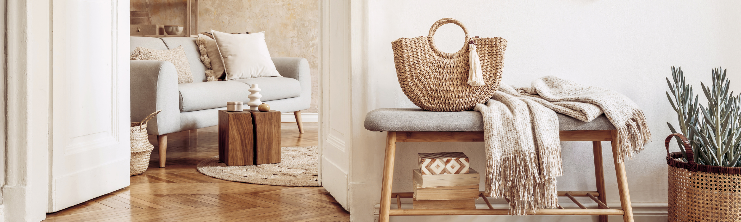 Cozy living room decor with a white sofa, small wooden side tables, decorative vases, and a woven handbag on a bench with blankets, surrounded by neutral tones and natural textures.