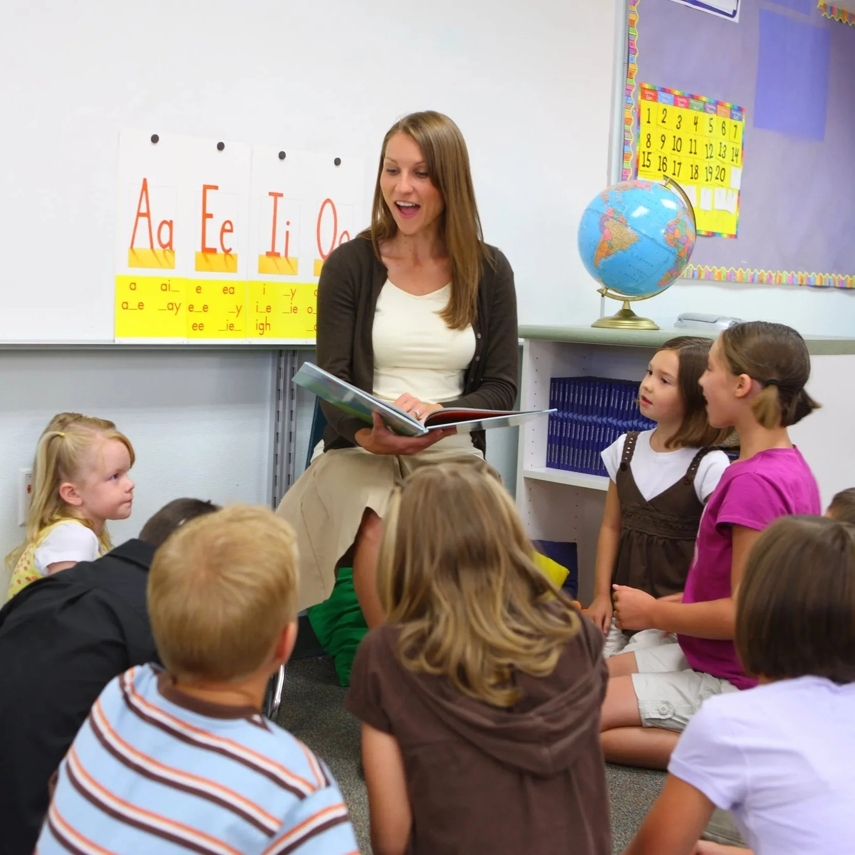 A teacher reads a book aloud to a group of elementary school children seated together in a classroom