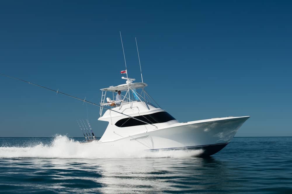 A white yacht cruising on calm ocean water under a clear blue sky.