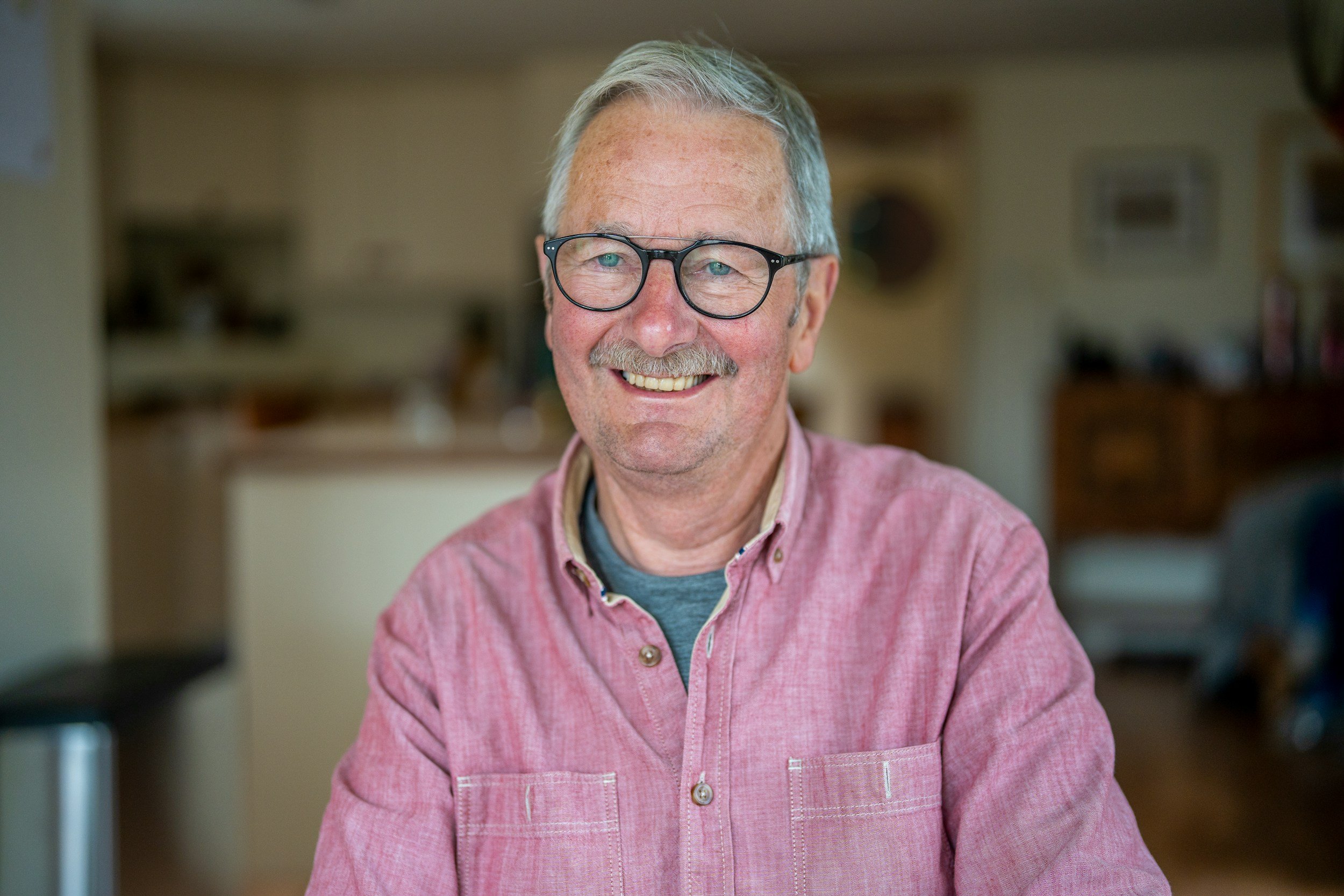 A middle-aged man with gray hair, glasses, and a beard smiling while wearing a pink button-down shirt.