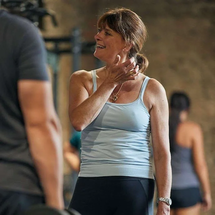 Smiling woman in a workout tank top talking to a man in a gym or fitness class setting.