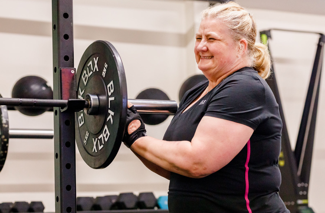 A woman lifting a barbell in a gym, smiling while exercising.