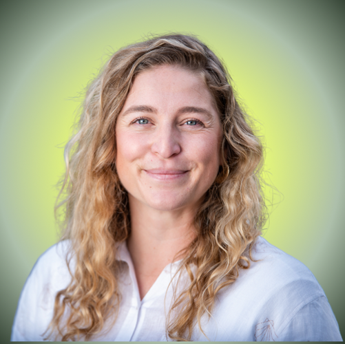 A woman with long, wavy blonde hair smiling and wearing a white shirt against a green background.