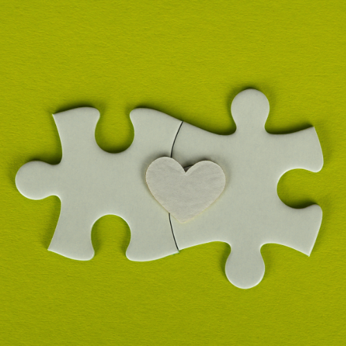 Two white puzzle pieces connected with a small white heart in the center, on a green background.