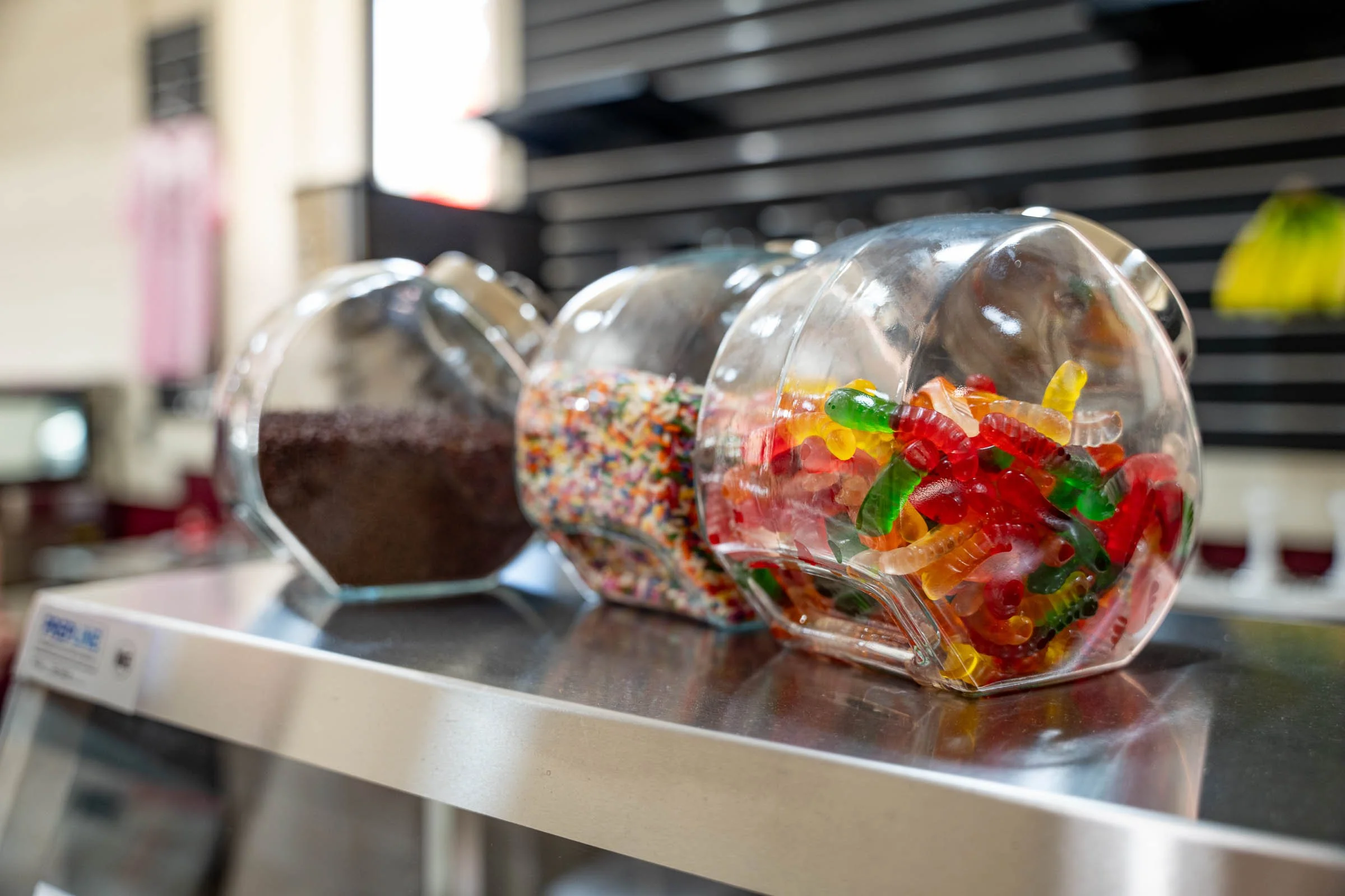 Clear bowl filled with colorful gummy worms on a scale in a store or bakery.