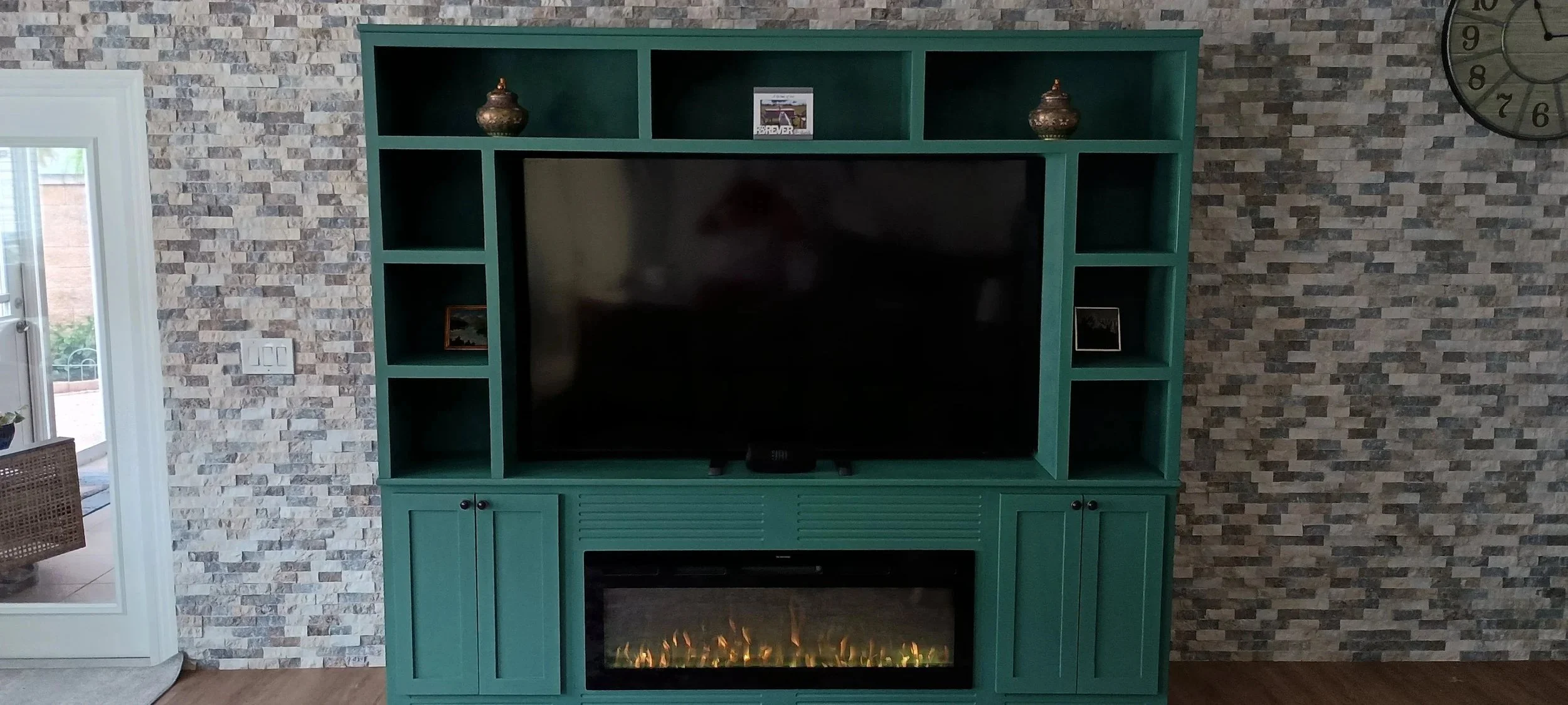 Custom Built-In Entertainment Center with Fireplace
A full-wall media unit combining open display shelving, framed cabinet storage, and a linear electric fireplace insert — finished in a rich forest green to anchor the room. Built for generations, no