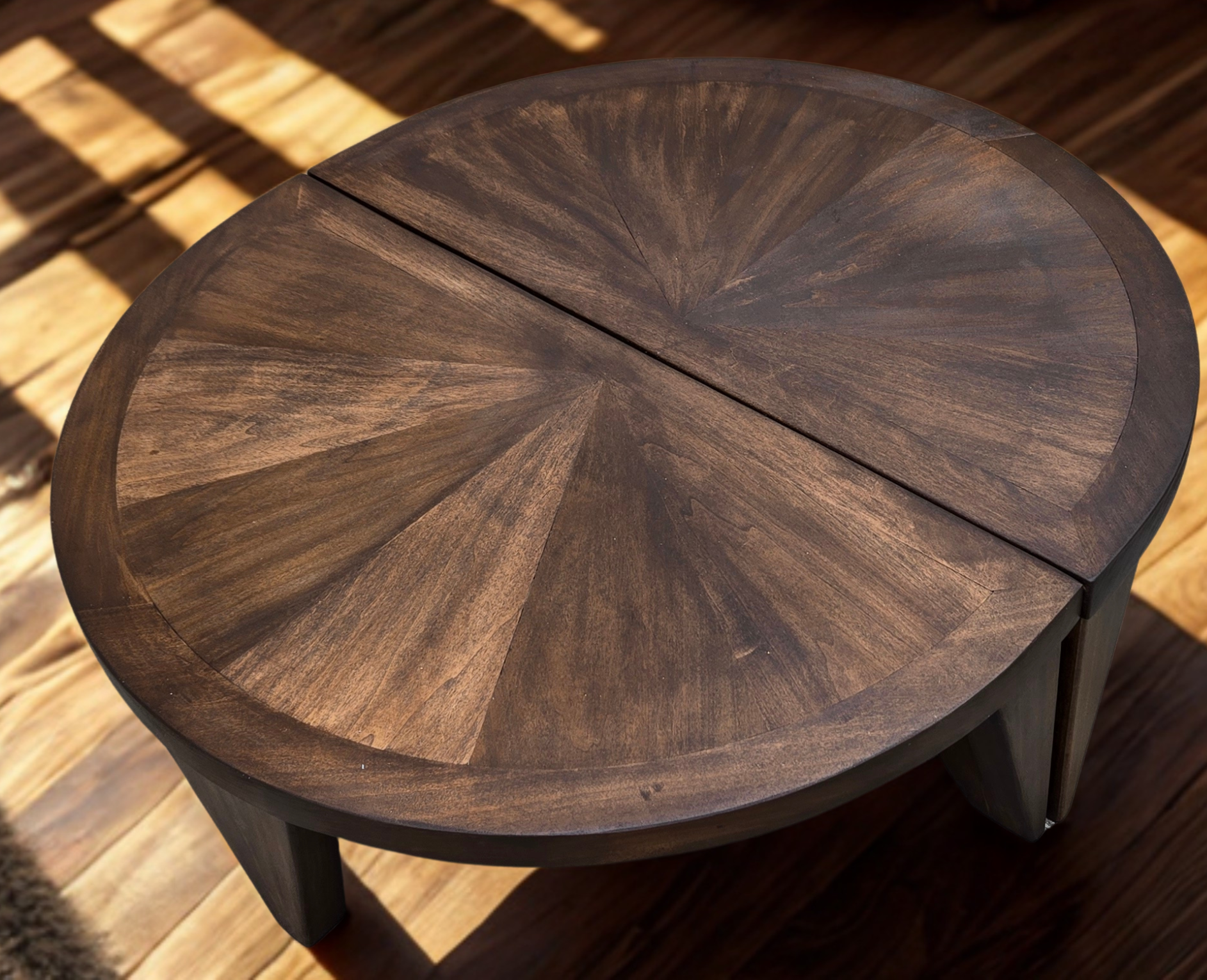 Close-up of a round wooden table with a geometric pattern on its surface, placed on a wooden floor with sunlight casting shadows.