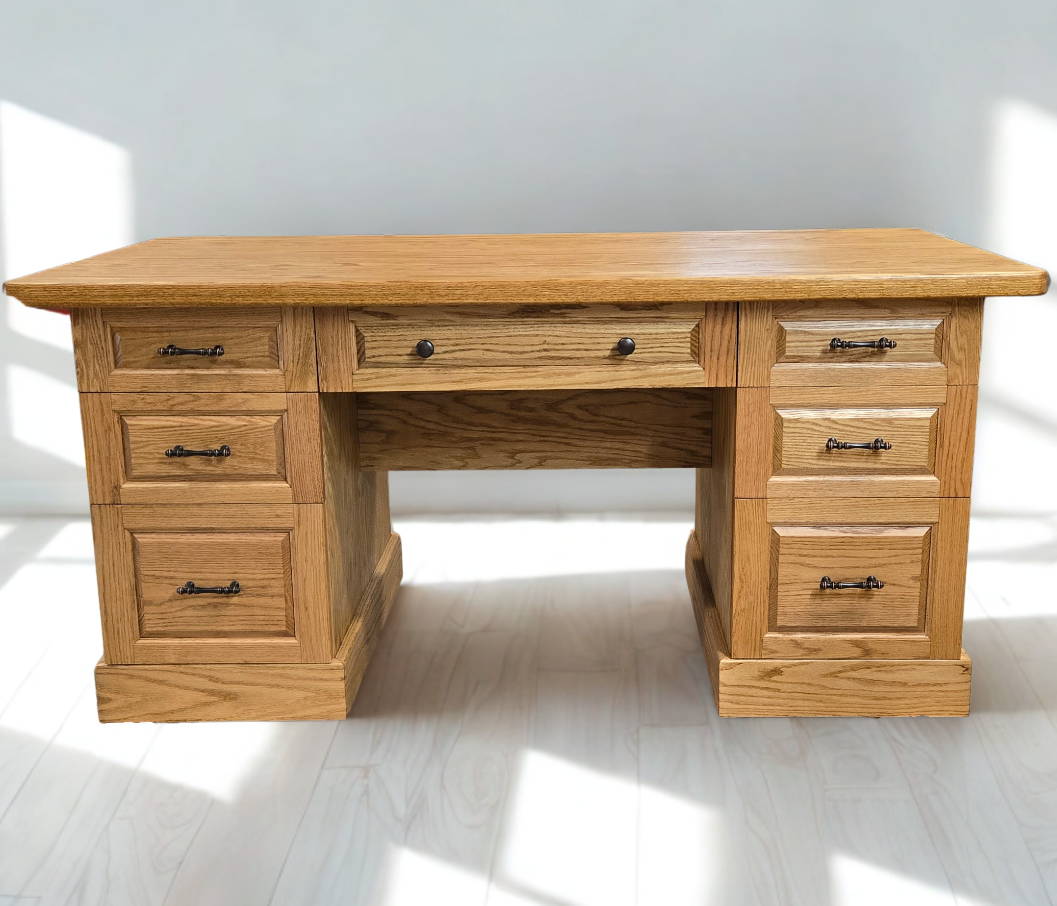 A wooden desk with multiple drawers against a plain wall, casting shadows on the floor.