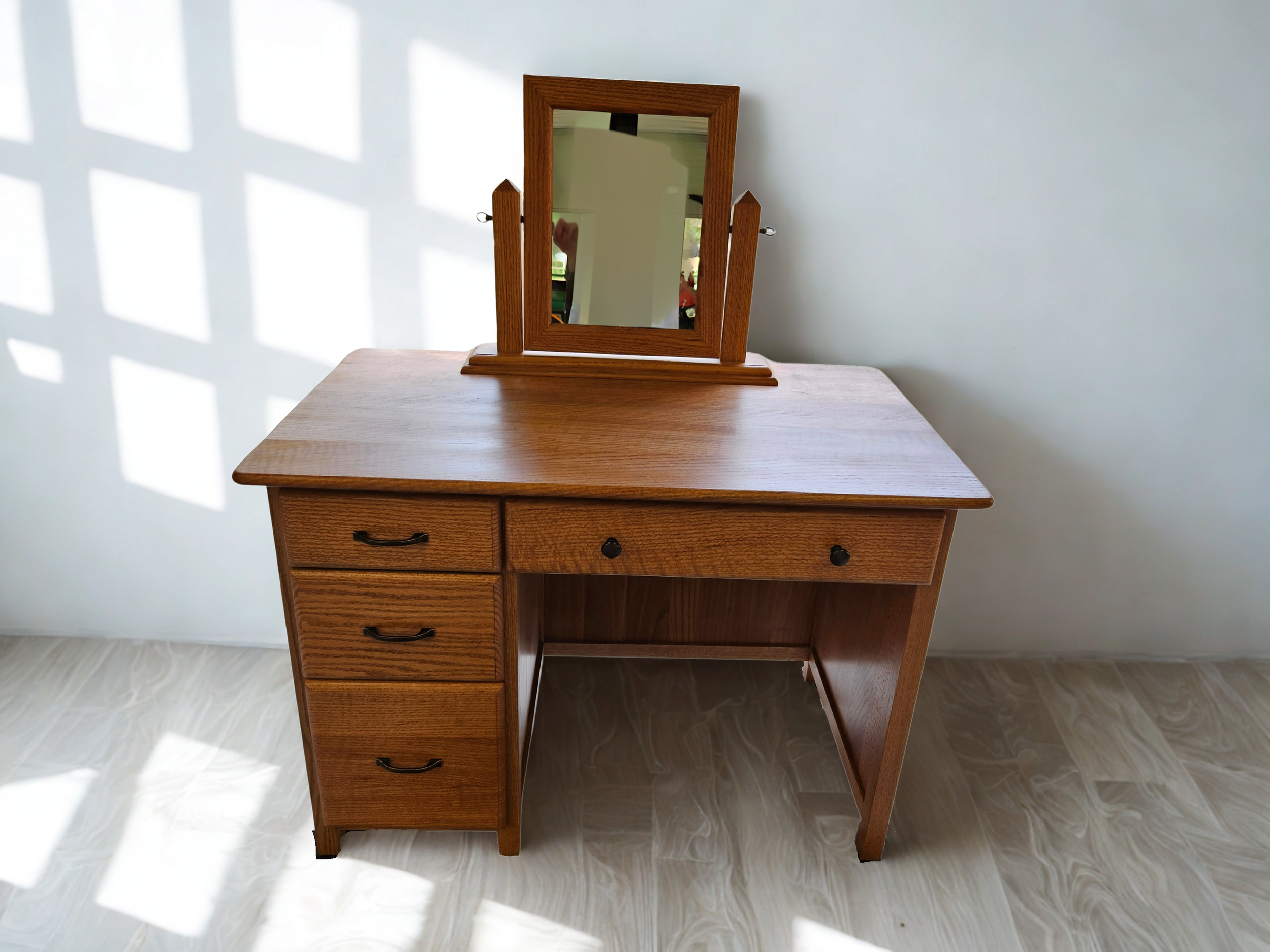 A wooden desk with multiple drawers and a small rectangular mirror on top, positioned against a white wall with shadow patterns.