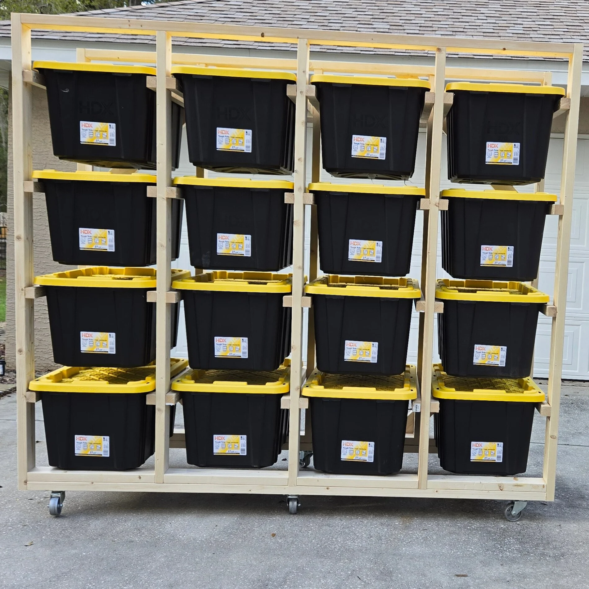 A mobile storage rack with multiple black and yellow plastic bins, each labeled with the HDX brand and storage information, set against a residential garage door.