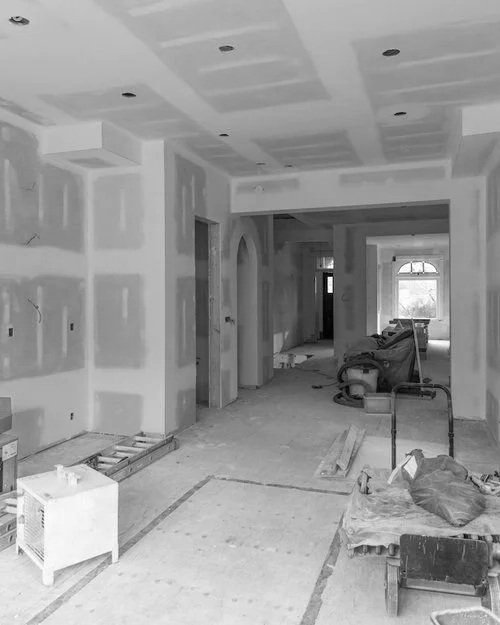 Interior of a house under construction with drywall panels, construction tools, and equipment present.
