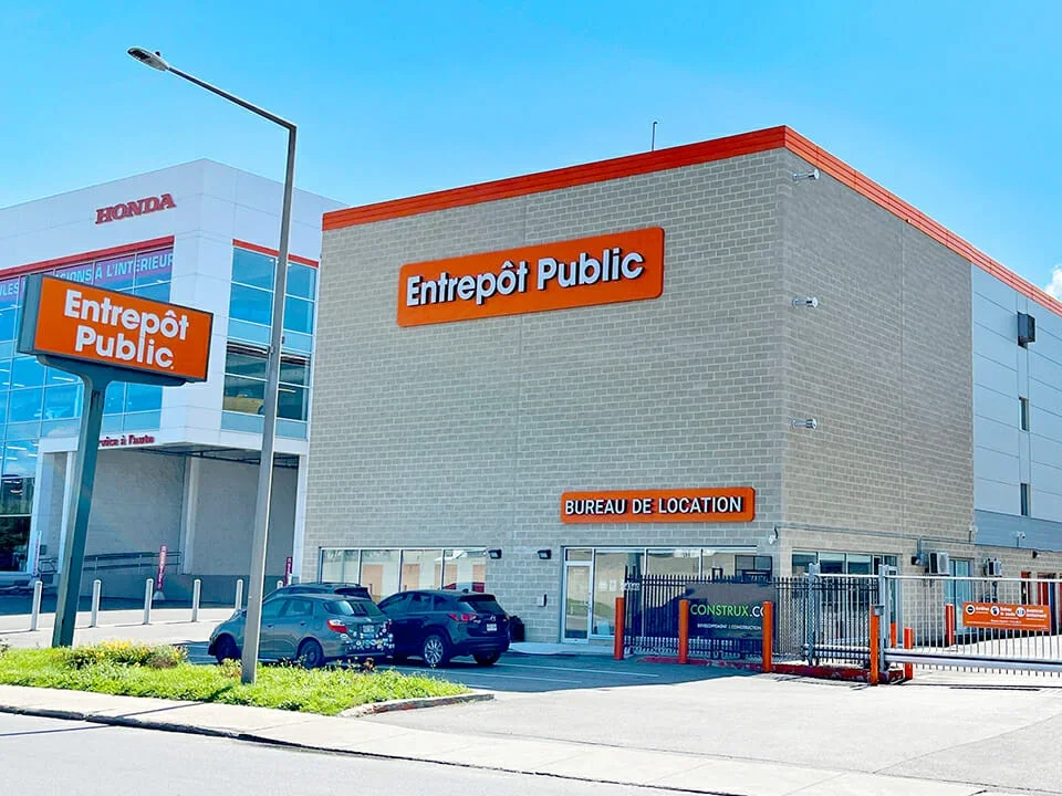 Public storage facility with signs in French, indicating outdoor parking with cars, a fenced area, and nearby buildings including a Honda dealership.