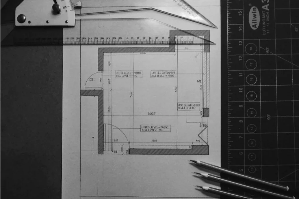 Architectural floor plan with various measurements, doors, and window placements, surrounded by drafting tools and pens.