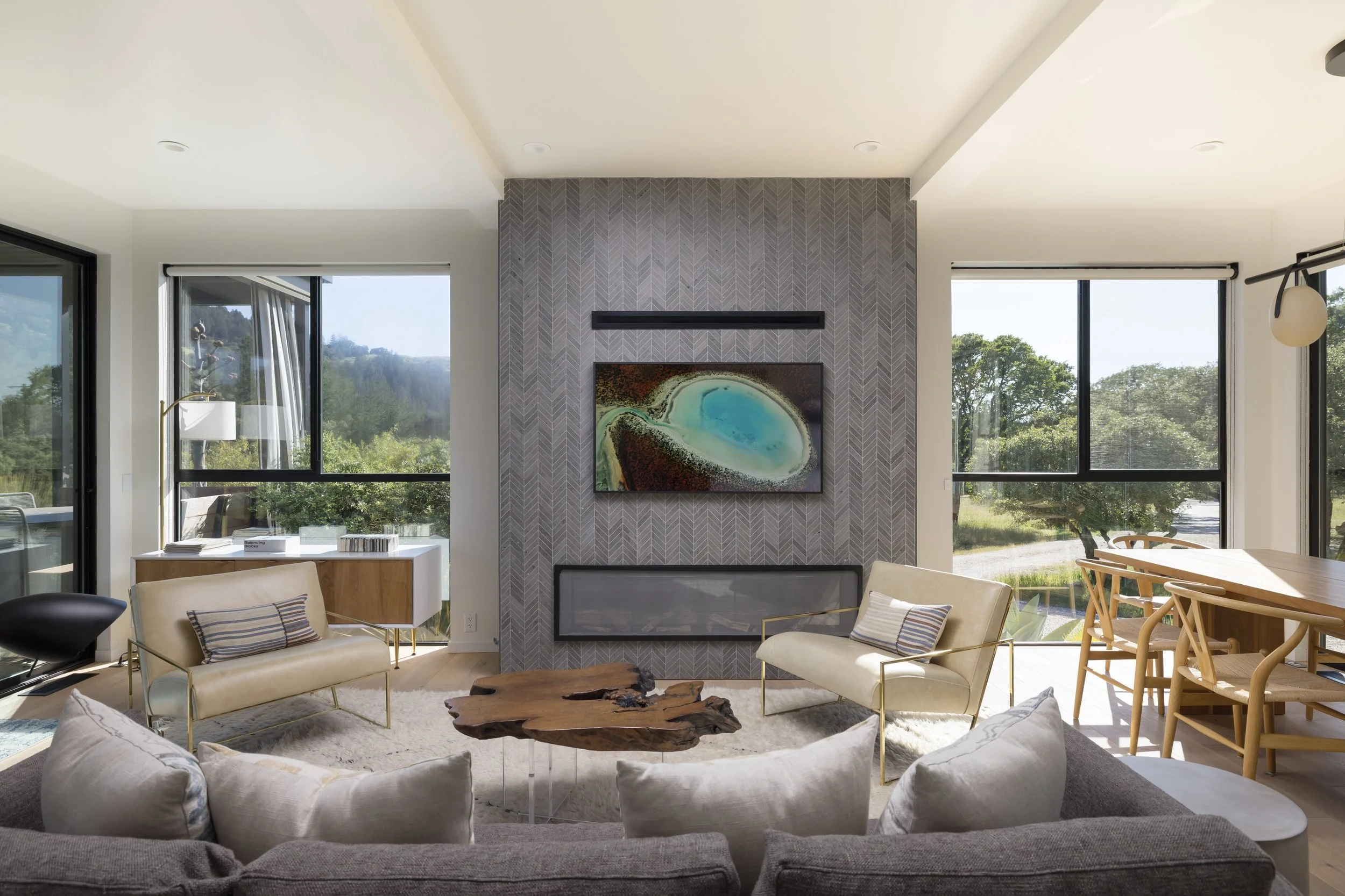 Living room with large windows, modern furniture, and a fireplace with artwork above