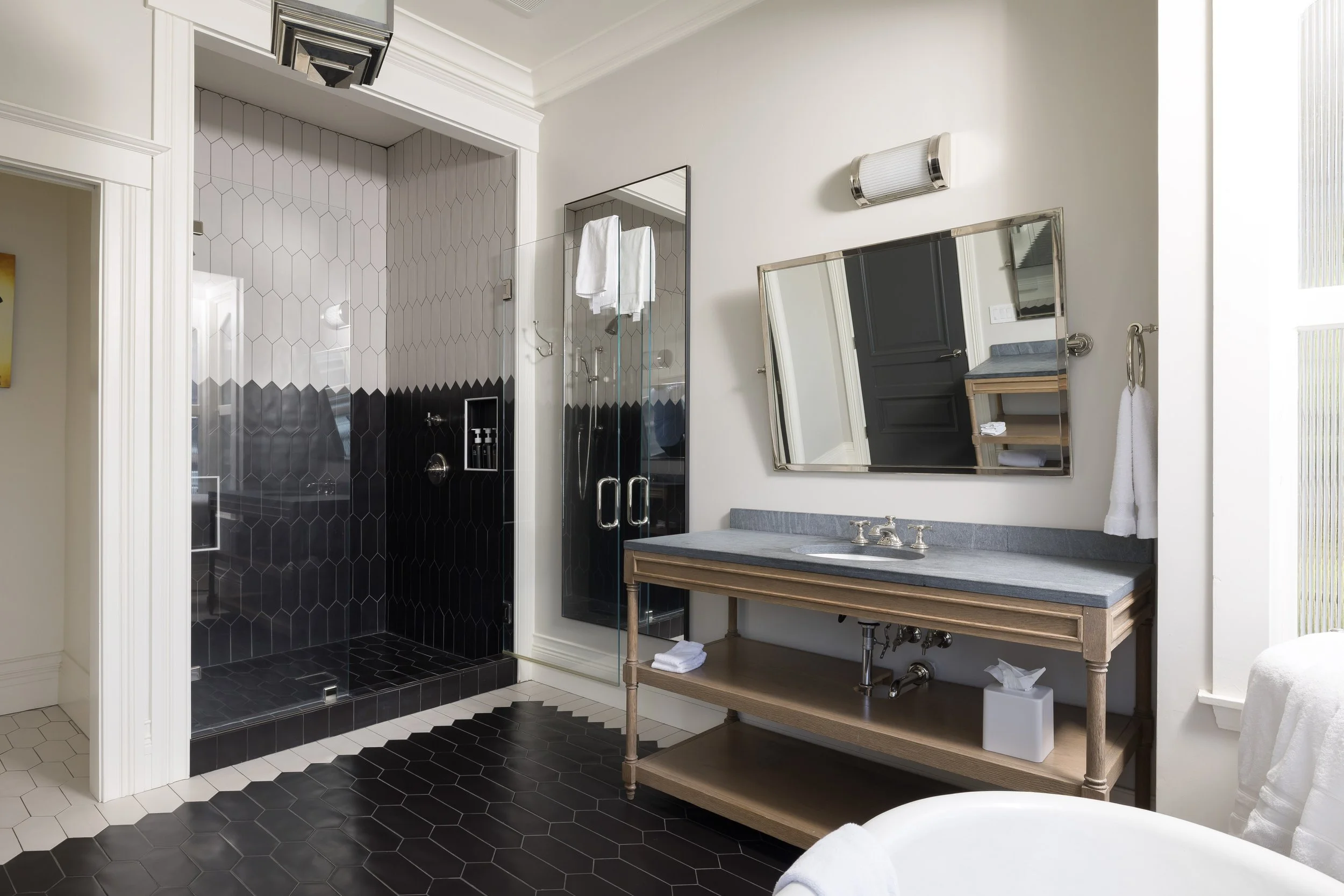 Bathroom with black hexagonal tiles in the shower area, a wooden vanity with a gray countertop, a mirror, towel, and a wall-mounted light fixture.