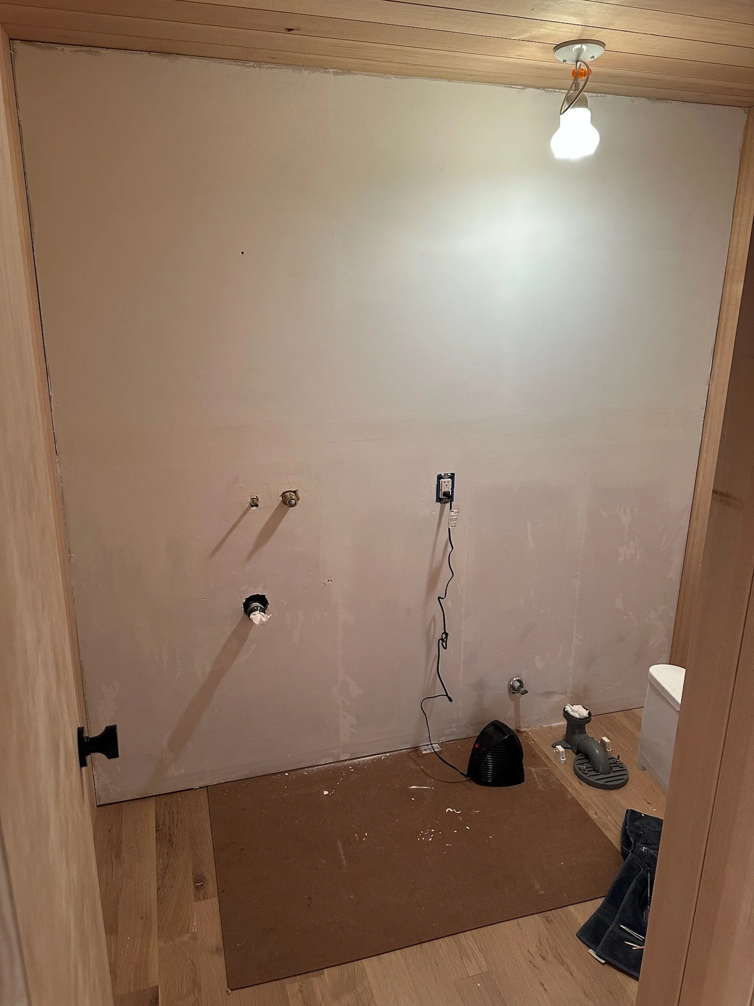 Unfinished room with a bare wall, exposed plumbing, and various tools and equipment on the floor, indicating ongoing construction or renovation work.