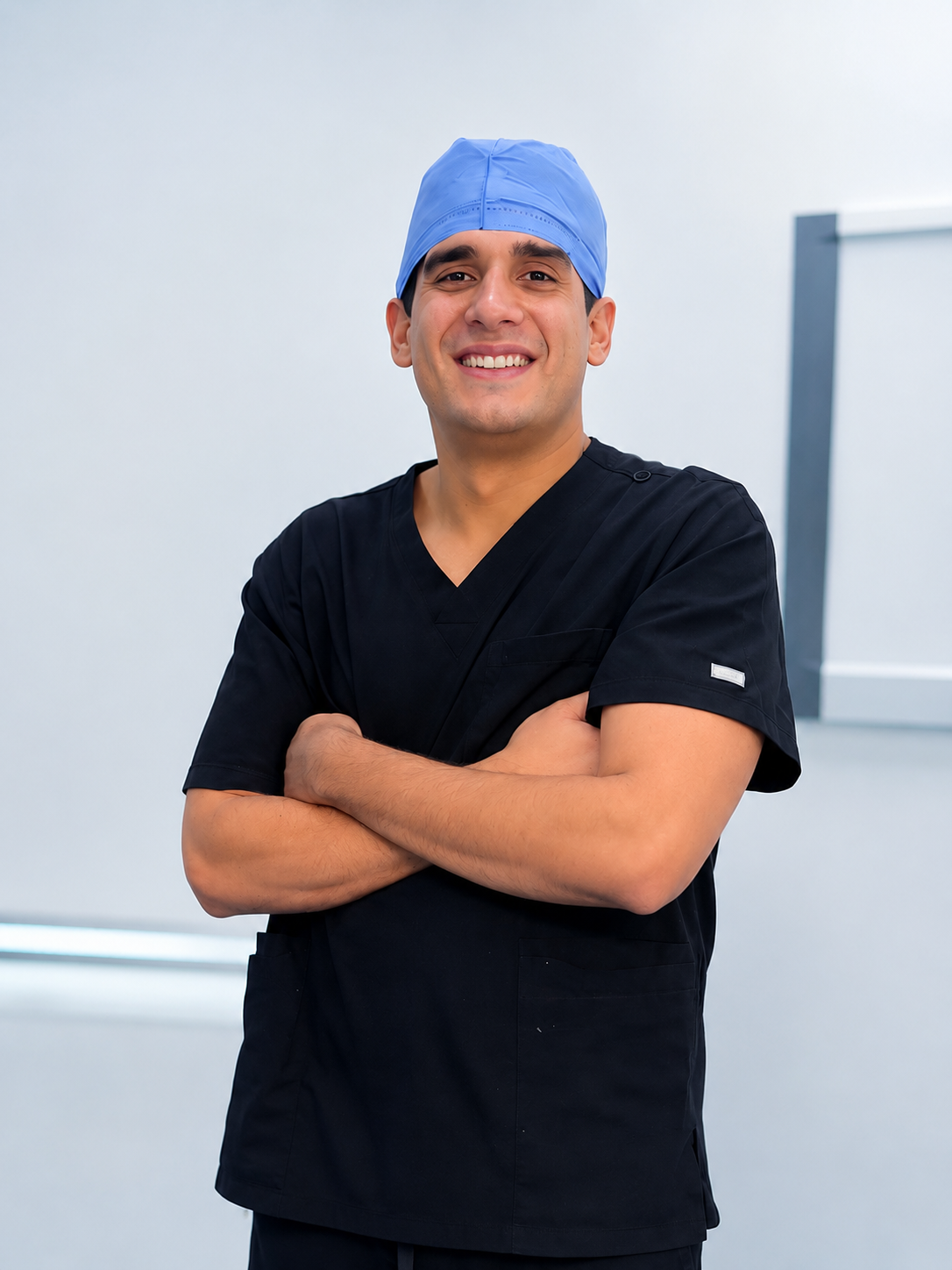Hombre médico o cirujano con gorra azul y ropa de scrubs negros sonriendo y con los brazos cruzados