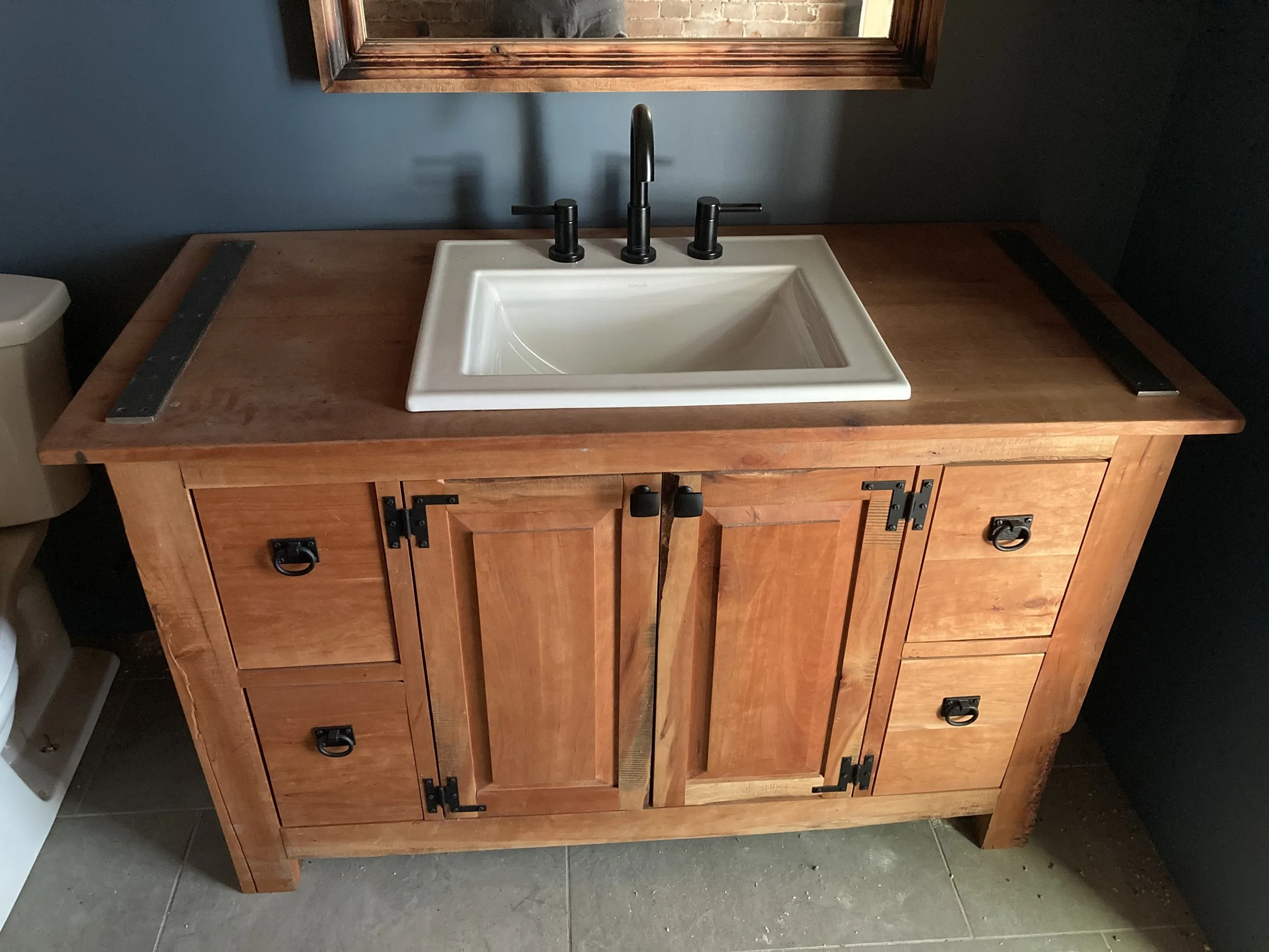 A cherry bathroom vanity with a rectangular white sink and black faucet fixtures on a wooden countertop. 