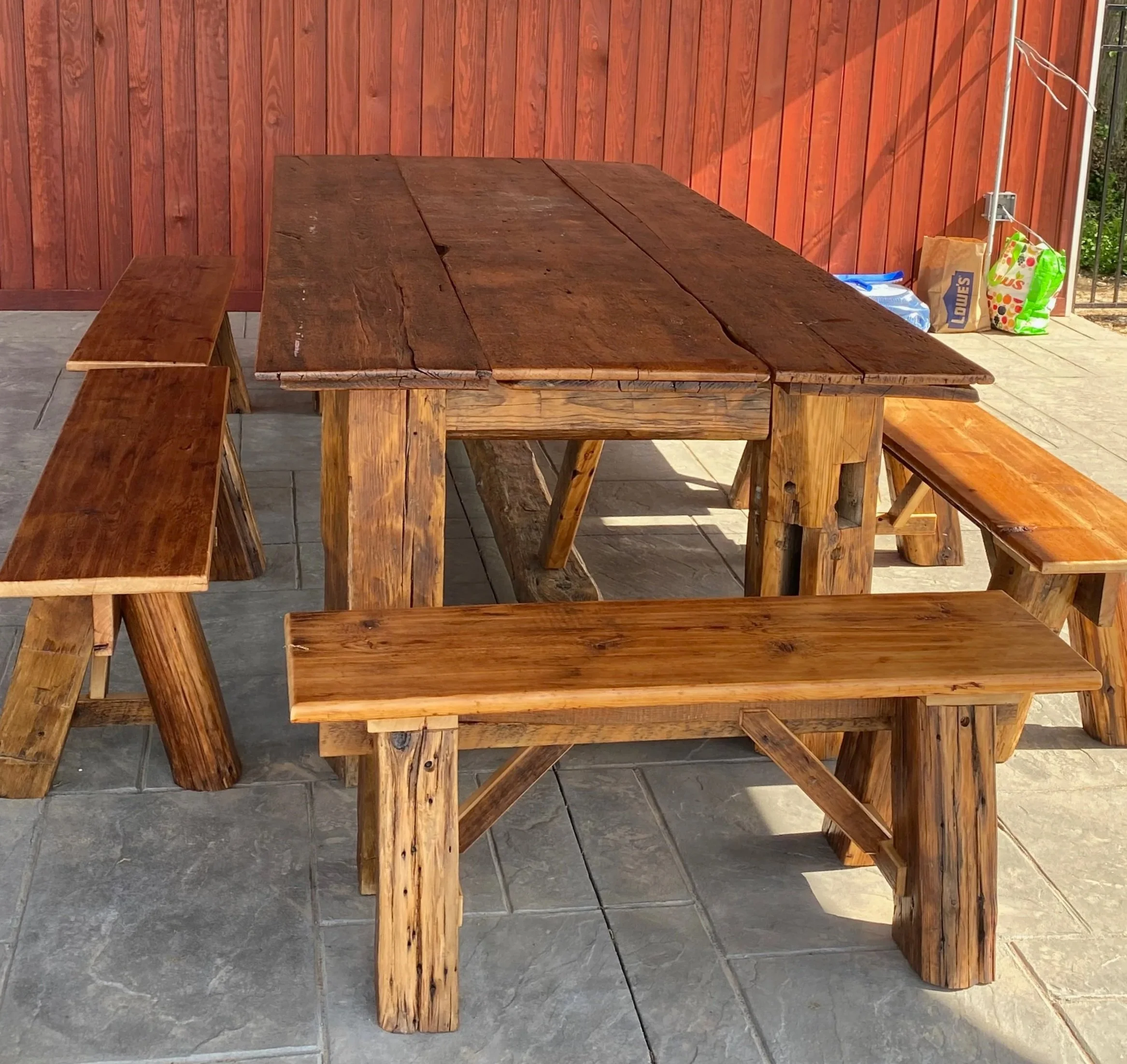 A wooden outdoor dining table with matching benches and chairs made from reclaimed lumber from an old barn.