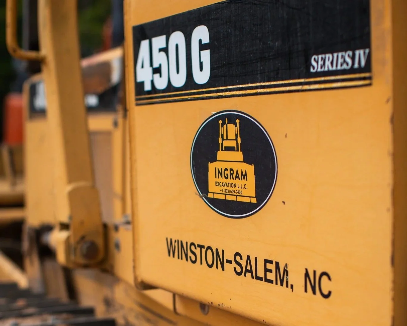 Close-up of a yellow construction equipment container with black and white labels, indicating 450 G, Series IV, and from Winston-Salem, NC. The container has a black circular logo of Ingram Excavation LLC.
