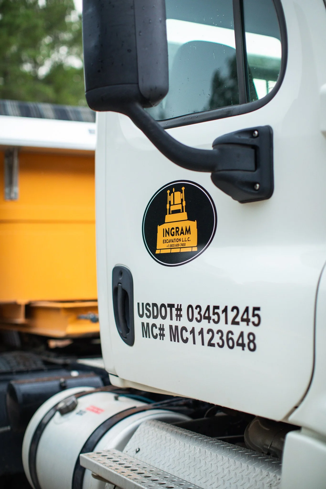 Close-up of a white utility truck's side showing a black and yellow sticker for Ingram Excavation LLC, with contact information and vehicle identification numbers.