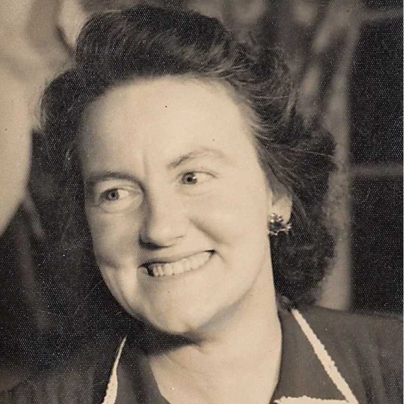 A black-and-white portrait of a woman smiling, with wavy hair and earrings, looking slightly to the side.