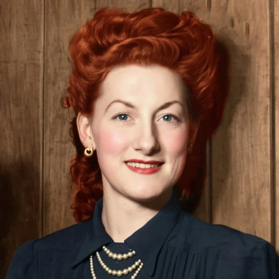 A colourised portrait of a woman with red hair, blue eyes, wearing gold earrings, a navy blouse, and layered pearl necklaces, standing in front of a wooden background.