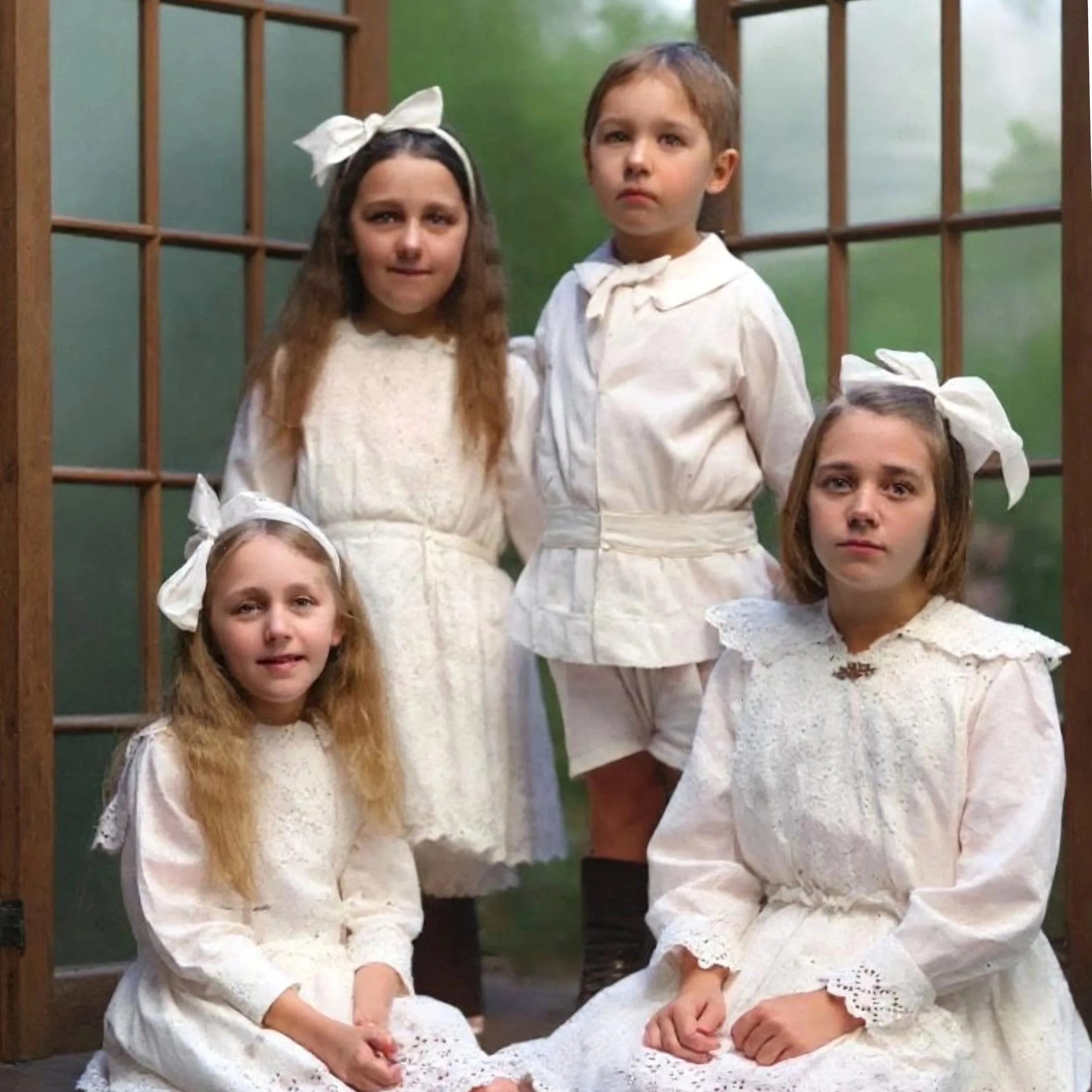 A colourised photo of a group of children in vintage clothes, sitting outdoors near a wooden fence with blurred green trees in the background.