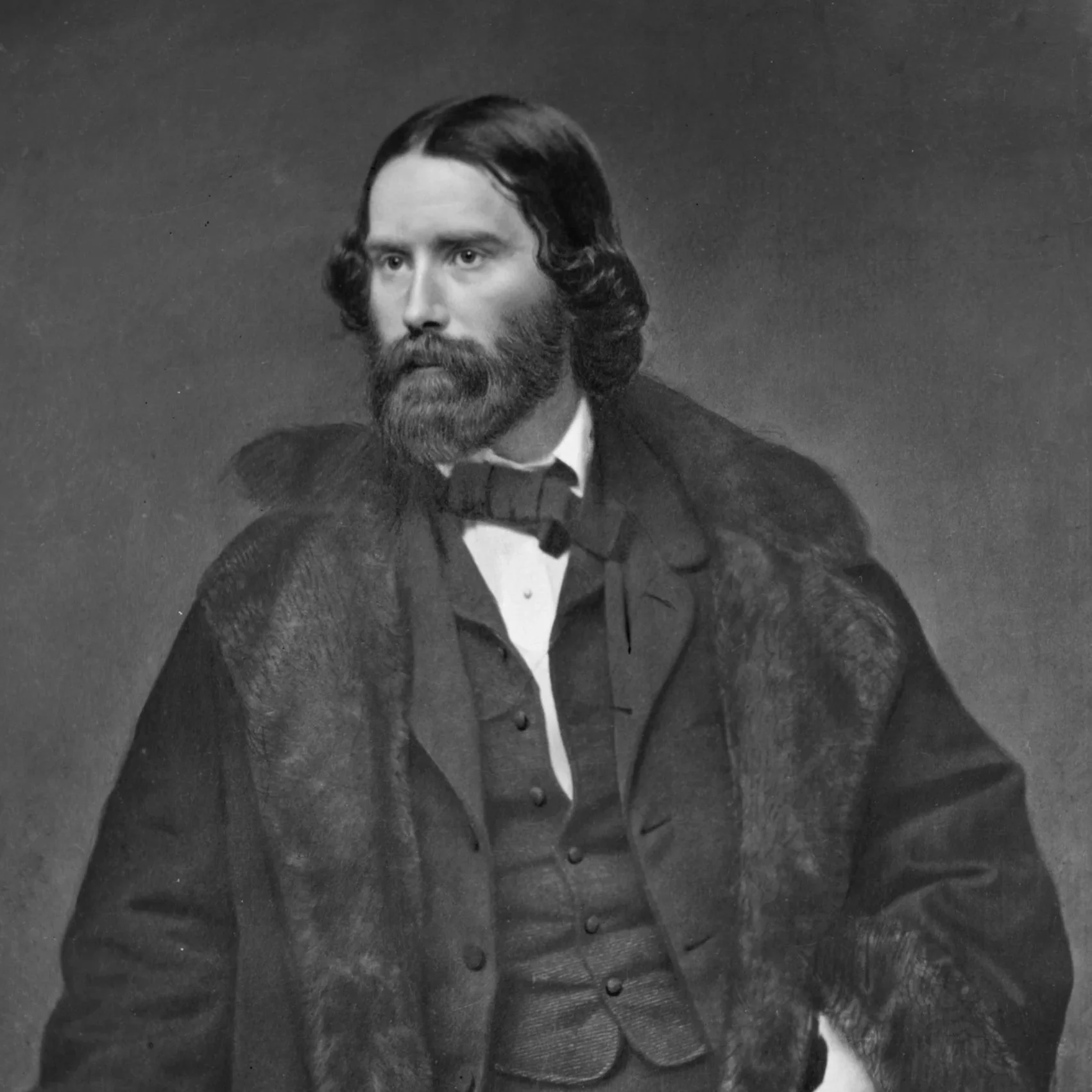 Black and white portrait of a man with a full beard and wavy hair, dressed in 19th-century formal attire including a coat with a wide collar and a bow tie.