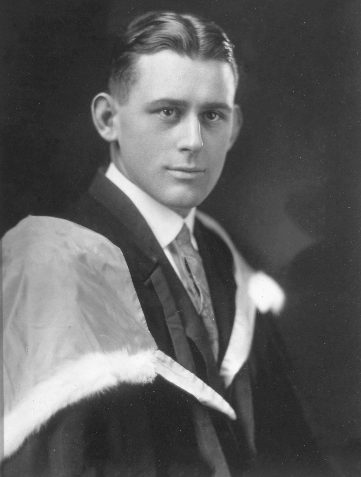 Black and white portrait of a young man in formal attire, wearing a tuxedo with a tuxedo jacket and a satin lapel, looking at the camera.
