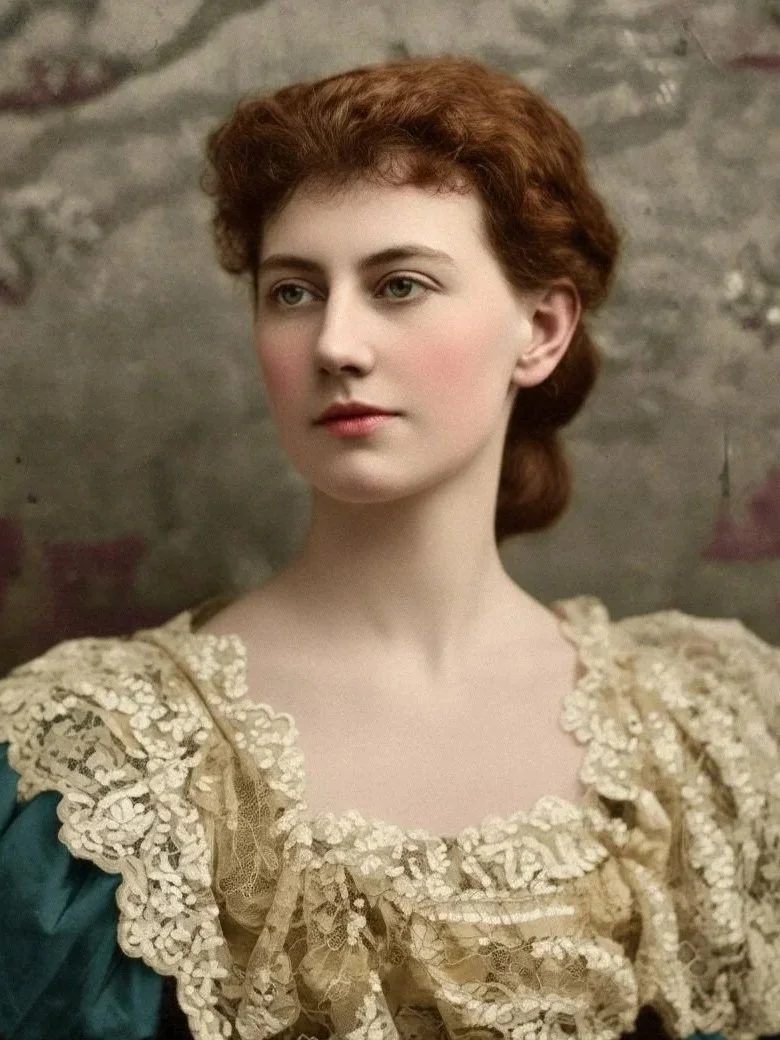 A colourised Portrait of a young woman with curly red hair wearing an ornate cream-colored lace dress, standing in front of a textured stone wall.