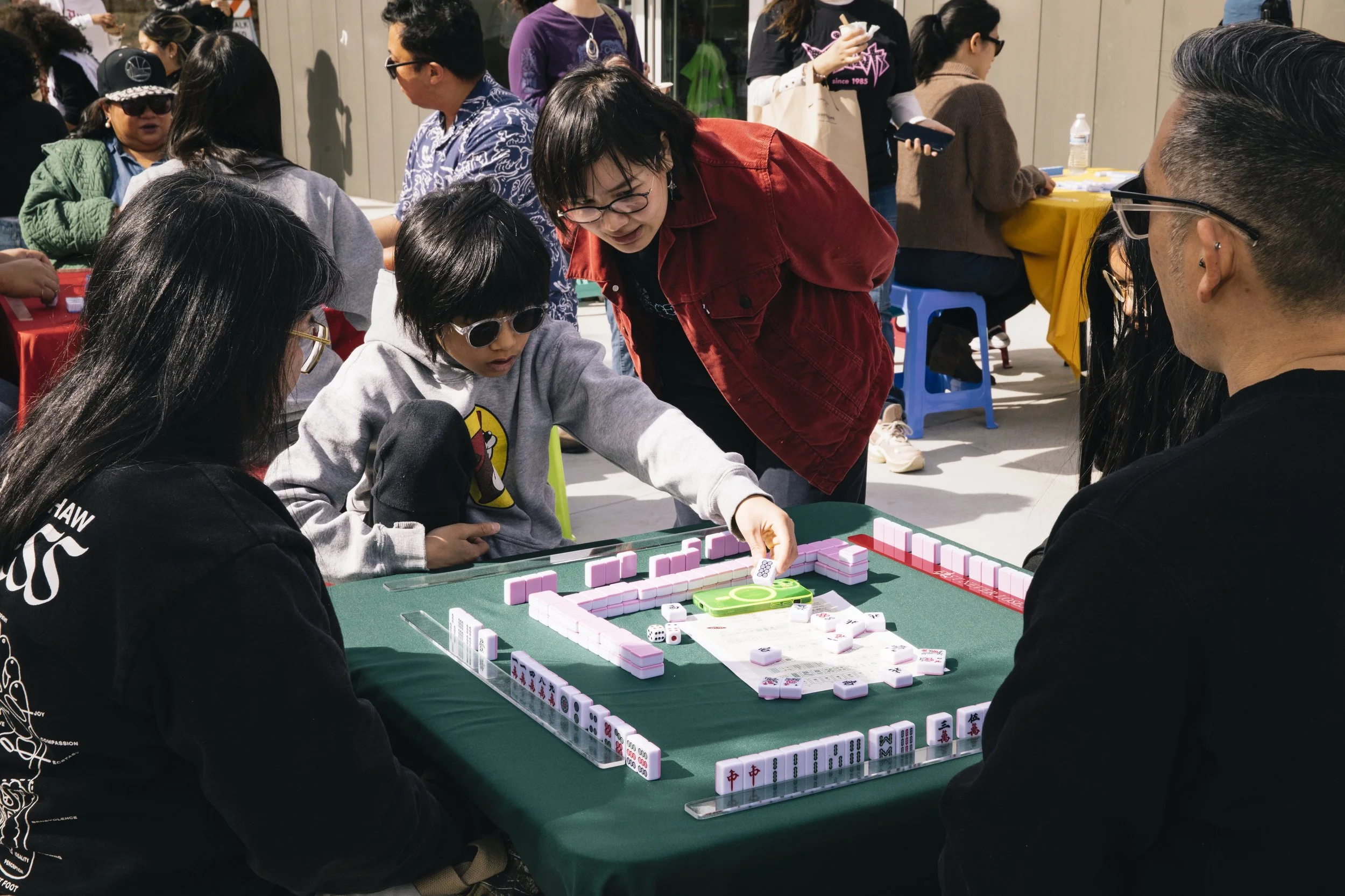 People playing Mahjong at a table outdoors during a crowded event.