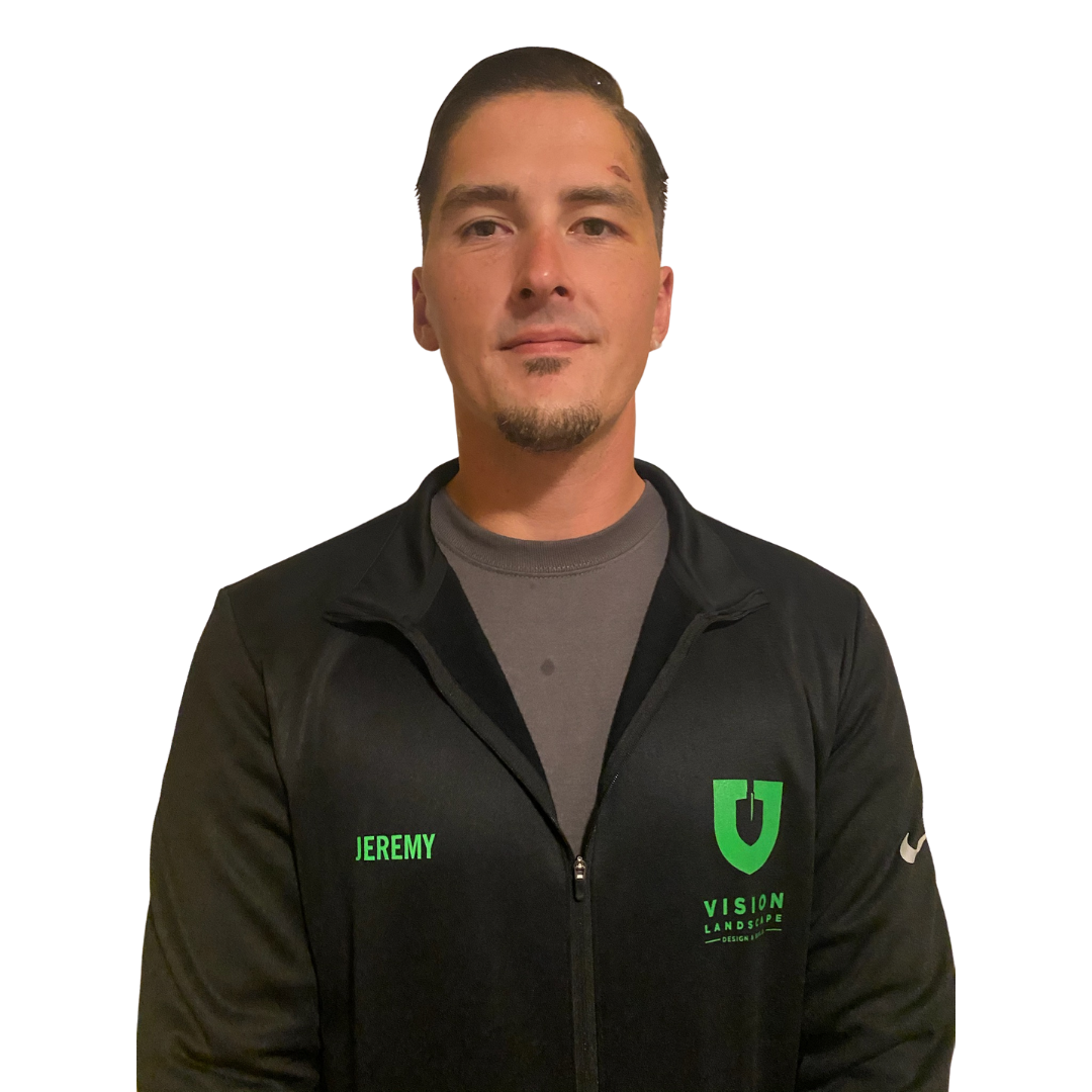 A man with short dark hair and a goatee, wearing a black jacket with green logos and text, standing against a white background.