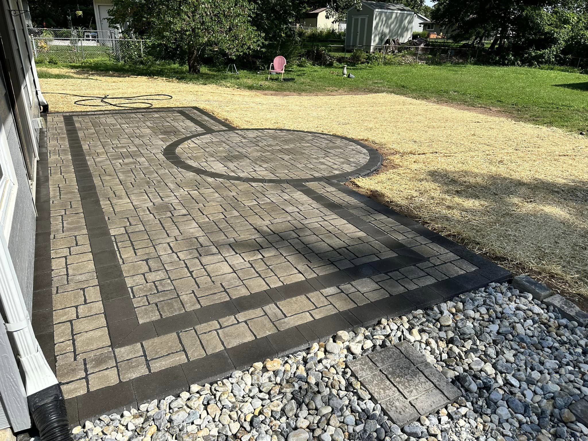 Backyard patio with brick pavers, a garden area with a small shed, trees, grass, and a pink chair.