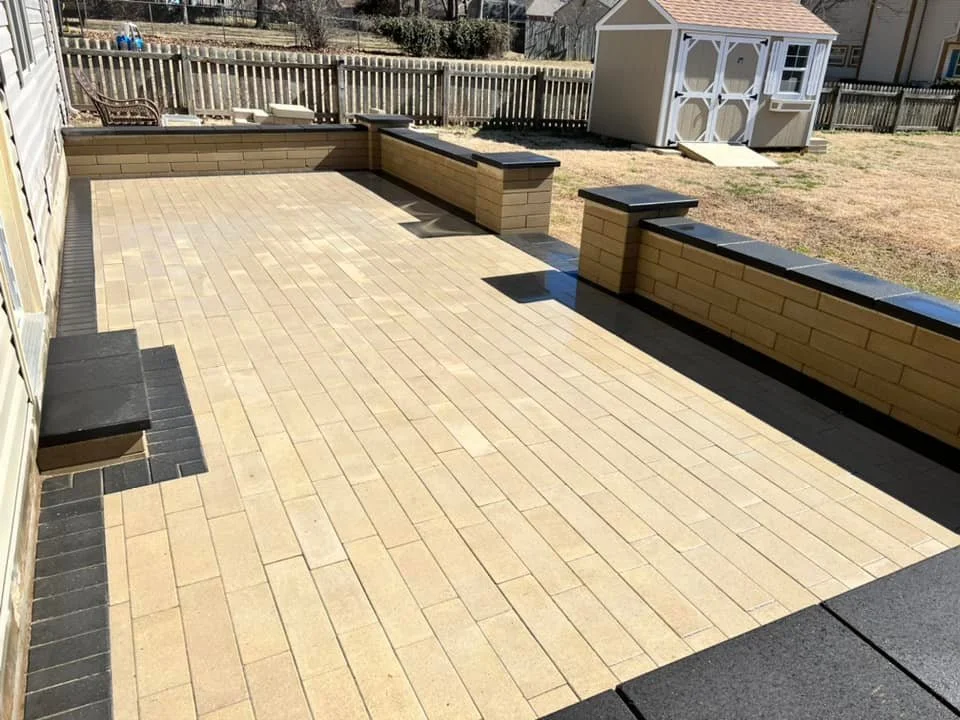 Empty backyard patio with brick and concrete wall benches, a shed, and a fenced yard with grass.