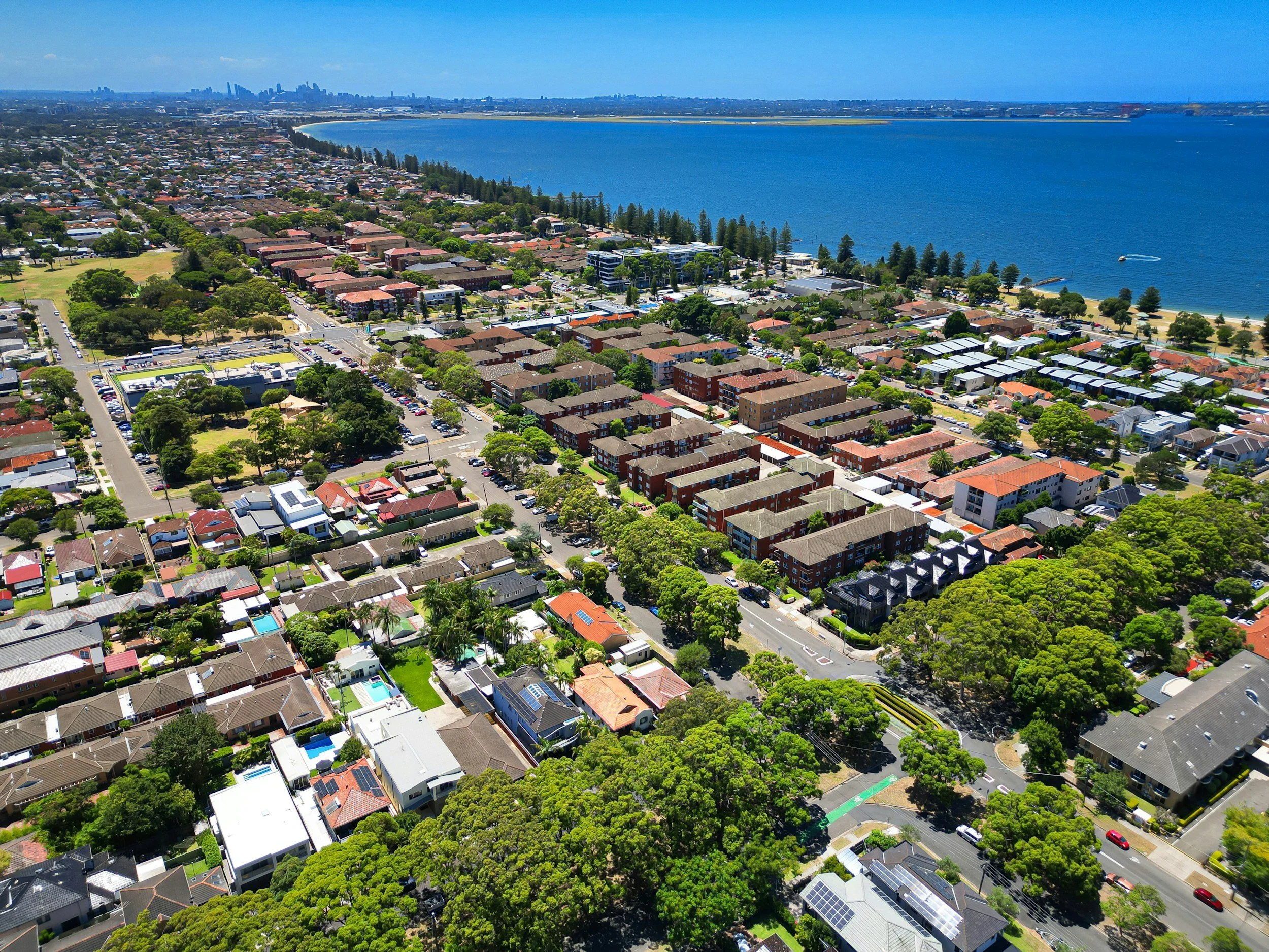 Aerial view of a coastal city with a beach along the shoreline, residential and commercial buildings, and a large body of water in the background.