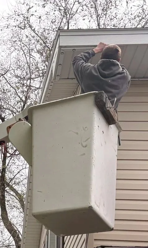 A man working on the roof of a house while standing in a bucket lift.