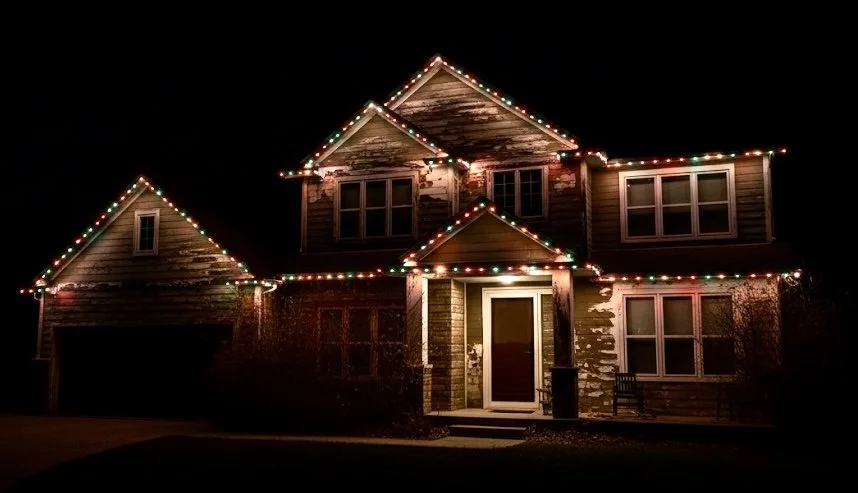 Two-story house decorated with colorful Christmas lights at night.