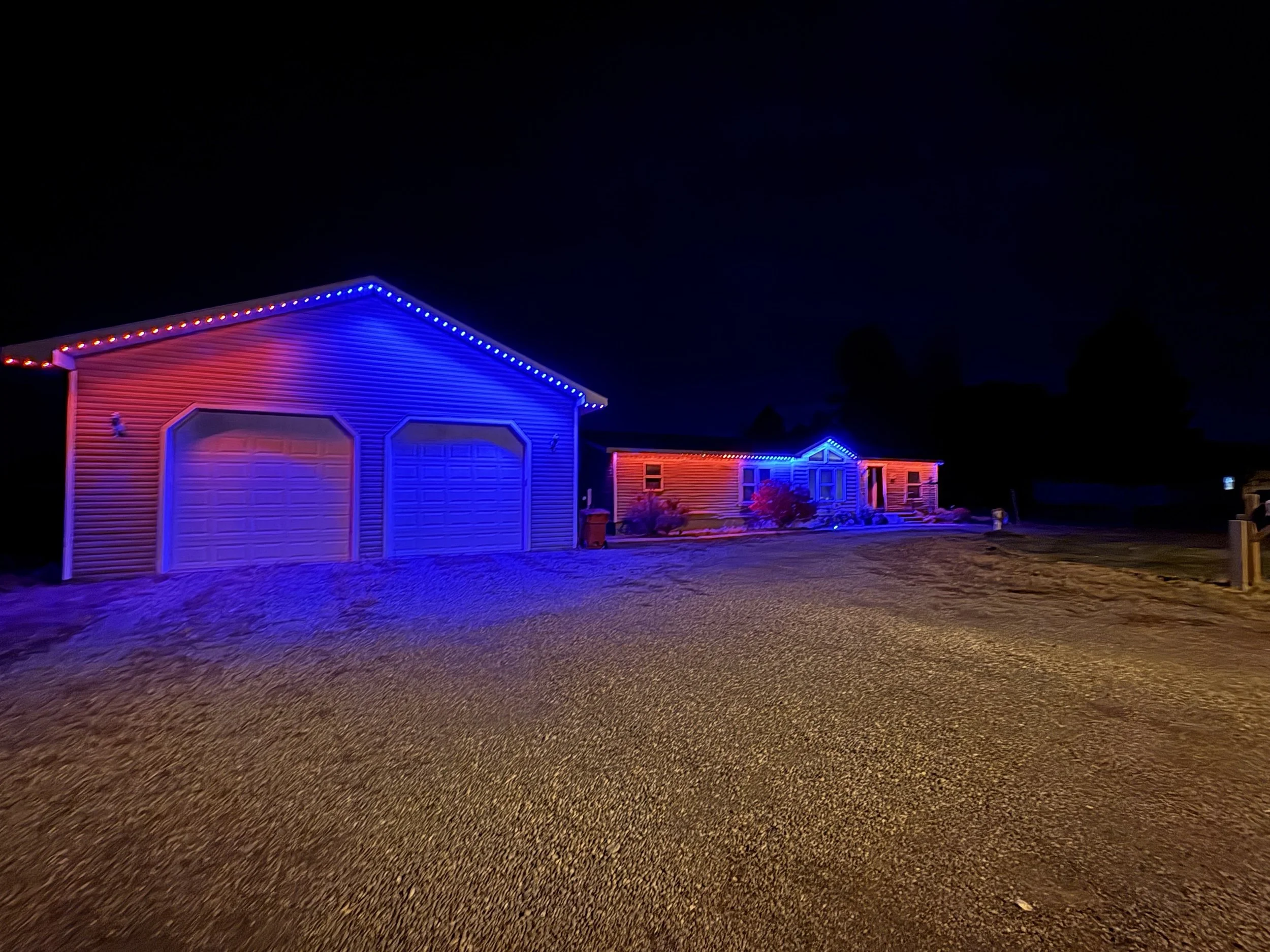A suburban house at night decorated with red, white, and blue LED Christmas lights outlining the roofline and windows.