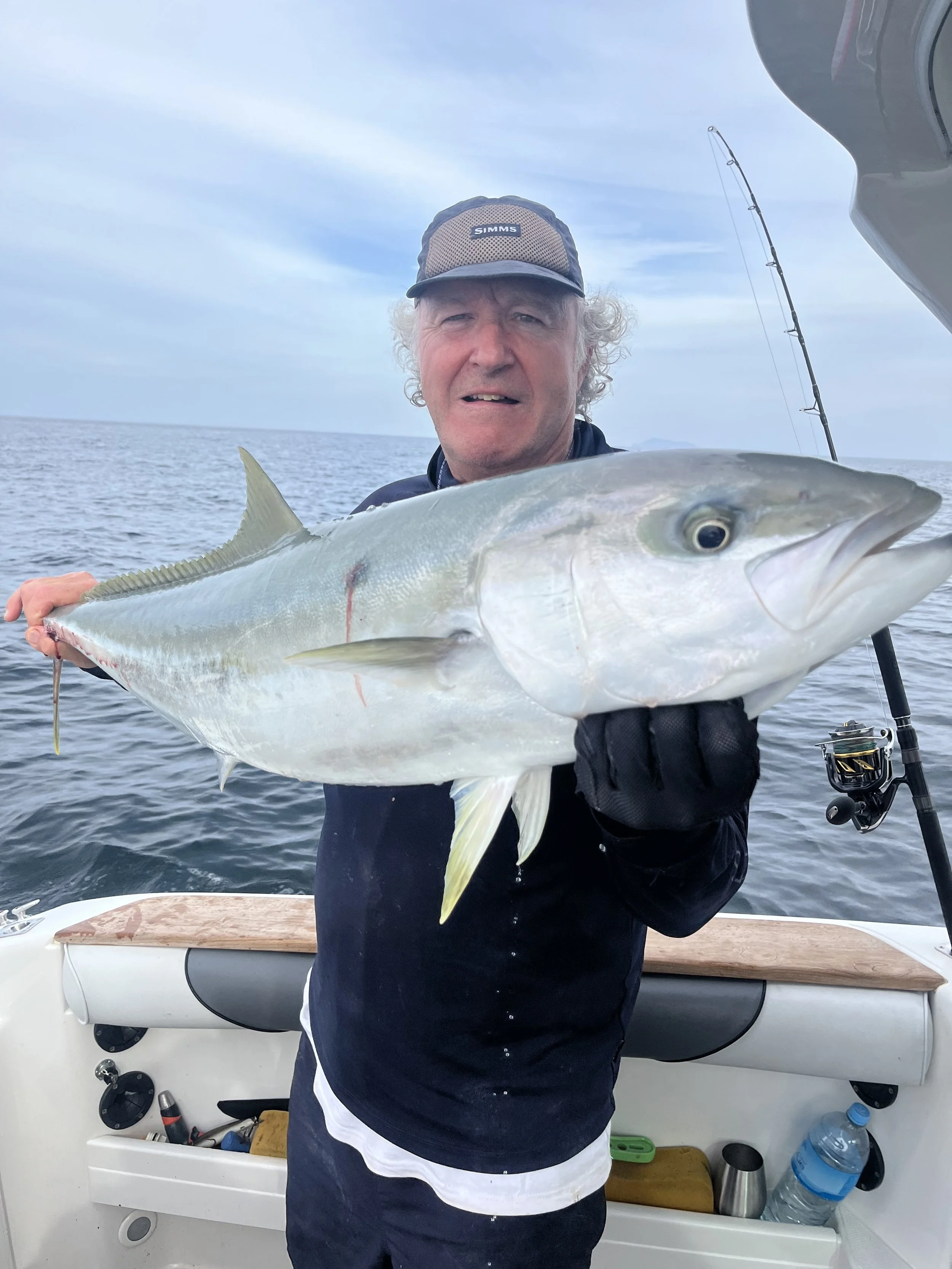 A man holding a large fish on a boat with ocean and sky in the background.