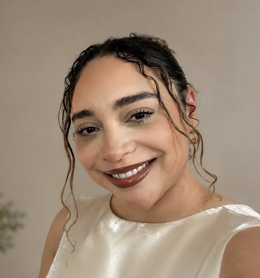 Close-up of a woman smiling with curly hair and wearing a sleeveless satin top.