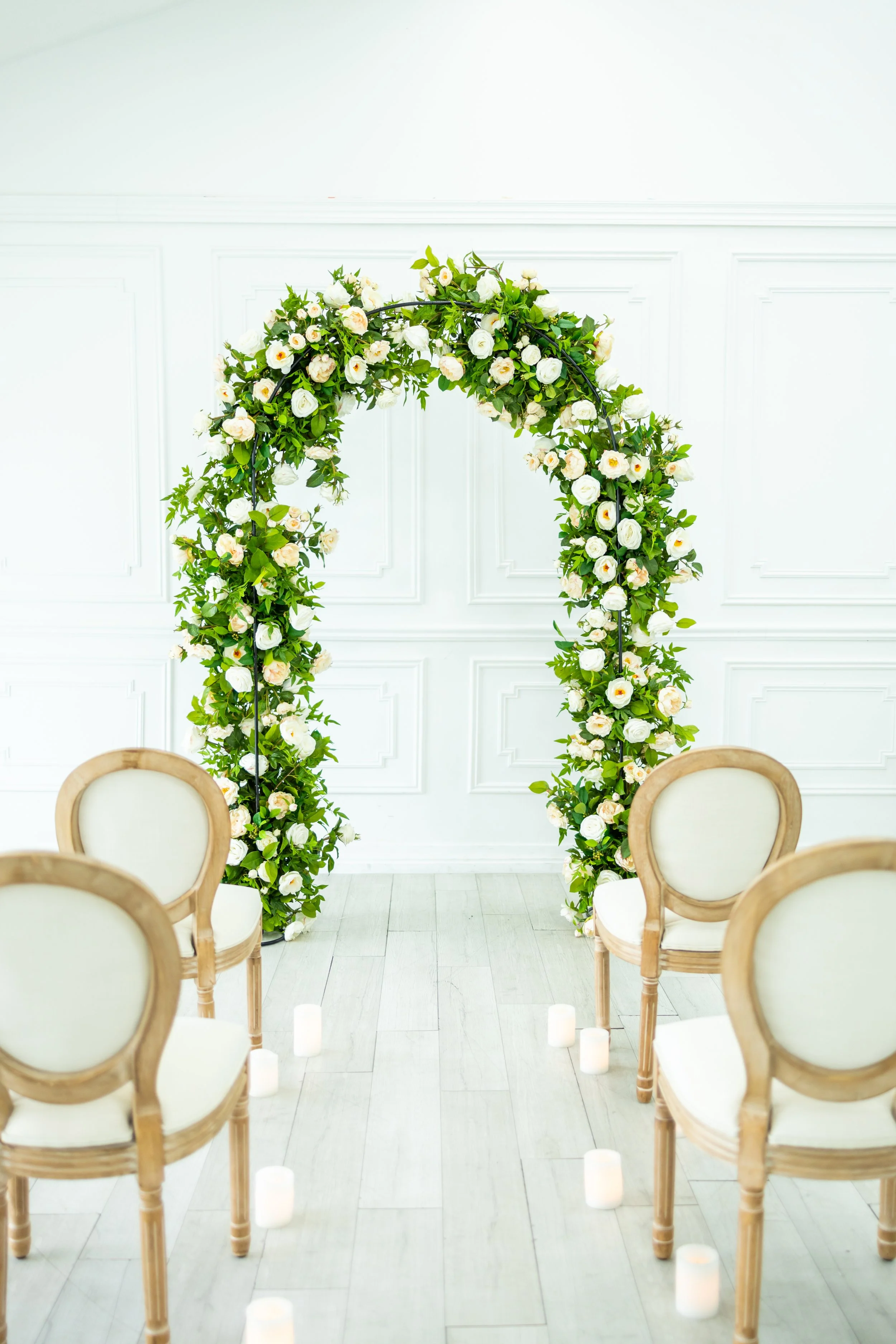 Elegant wedding ceremony setup with a flower arch and chairs arranged for guests, with candle lights on the floor.
