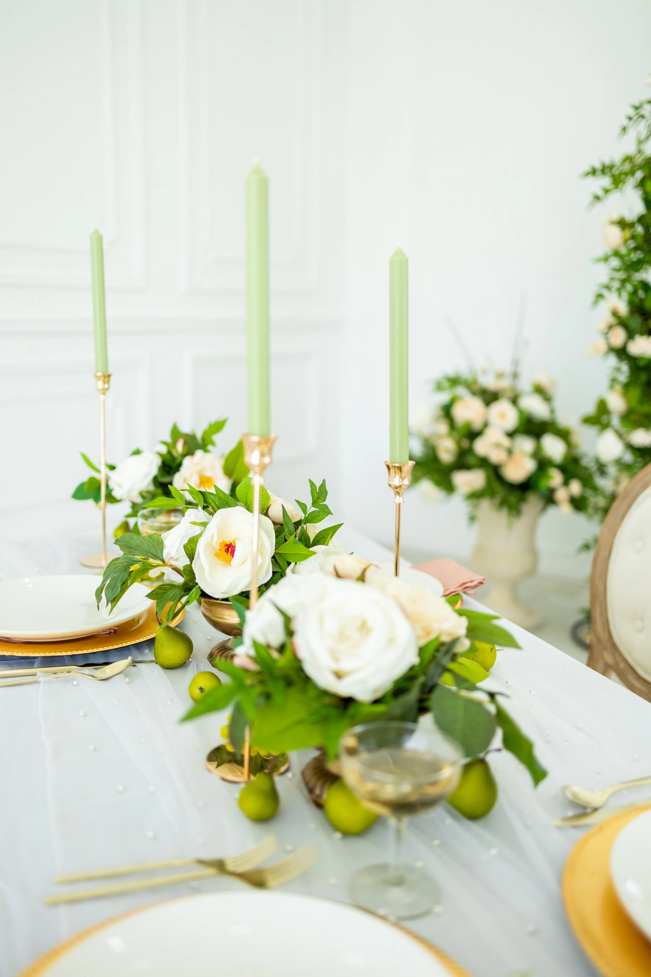 Elegant table setting with white flowers, green candles, and gold accents for a special event or celebration.