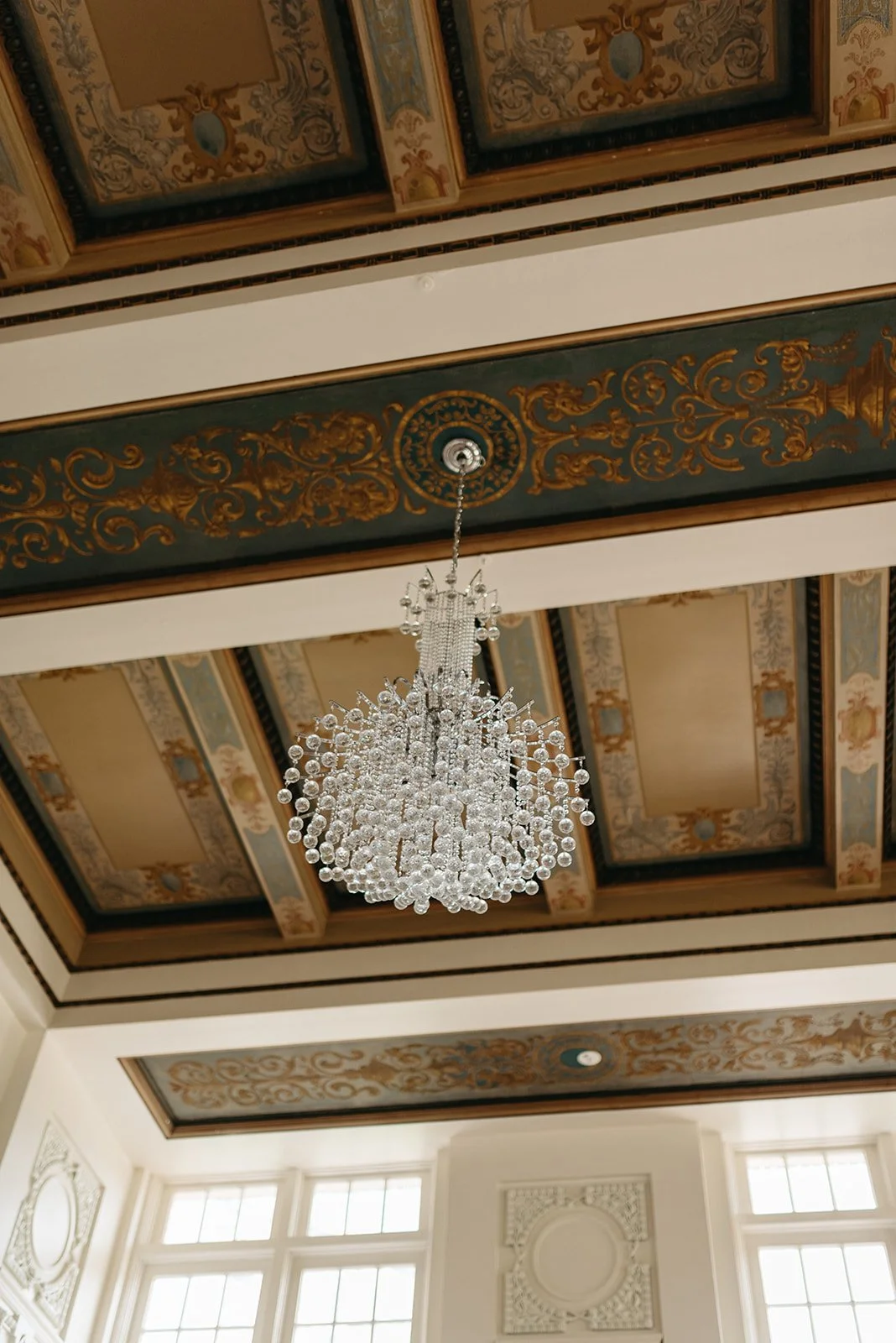 Elegant room ceiling featuring an ornate gilded plasterwork design with a large, sparkling chandelier hanging in the center.
